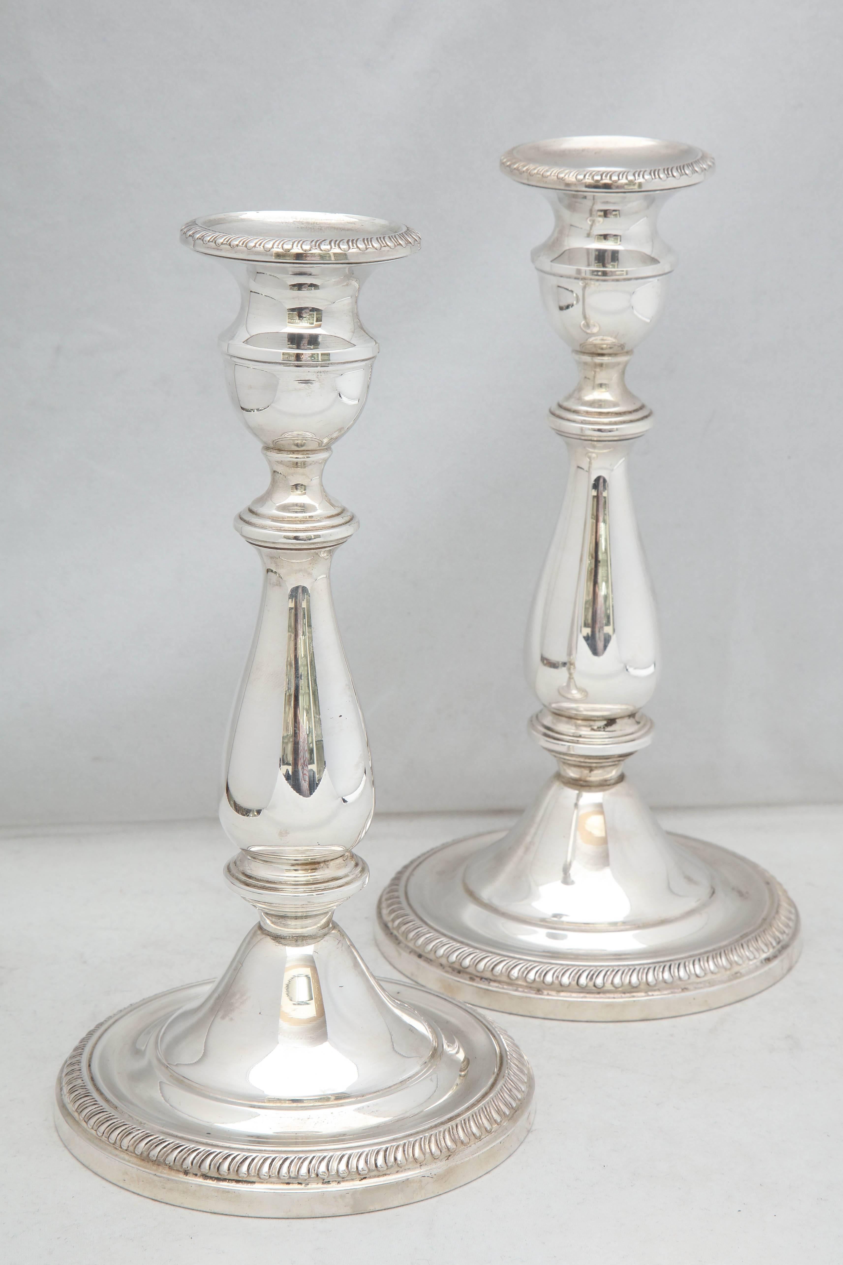 Pair of tall, sterling silver, Empire style candlesticks, The Mueck Carey Co. Inc., New York, circa 1930s. Measure: 9 inches high x 4 3/4 inches diameter across base of each. Weighted. Border of each candlestick base is decorated with a reeded
