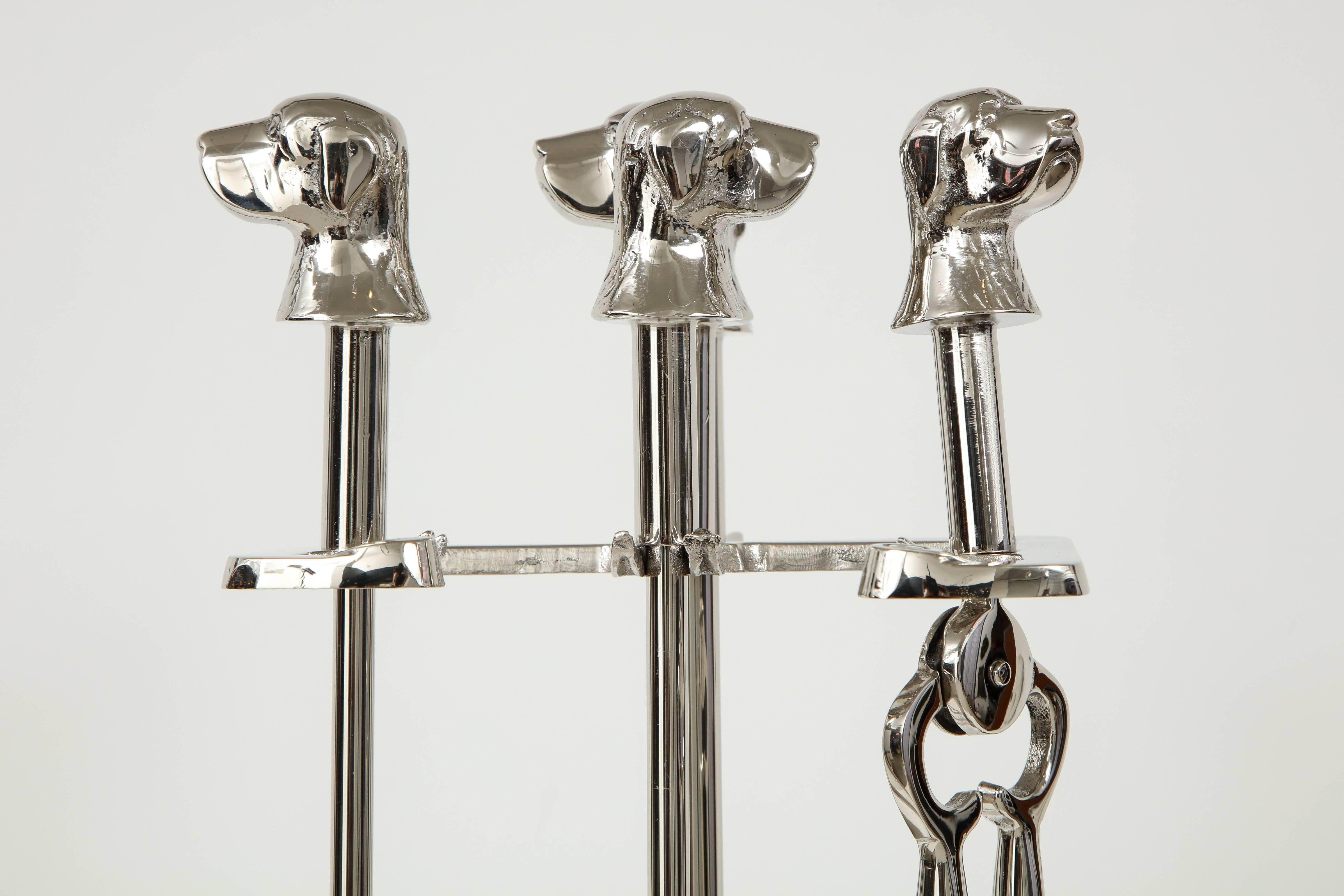 Set of Art Deco polished nickel fire tools with stylized dog head finials, most likely retriever or labrador breed. Set includes stand, shovel, poker, tongs, and broom.