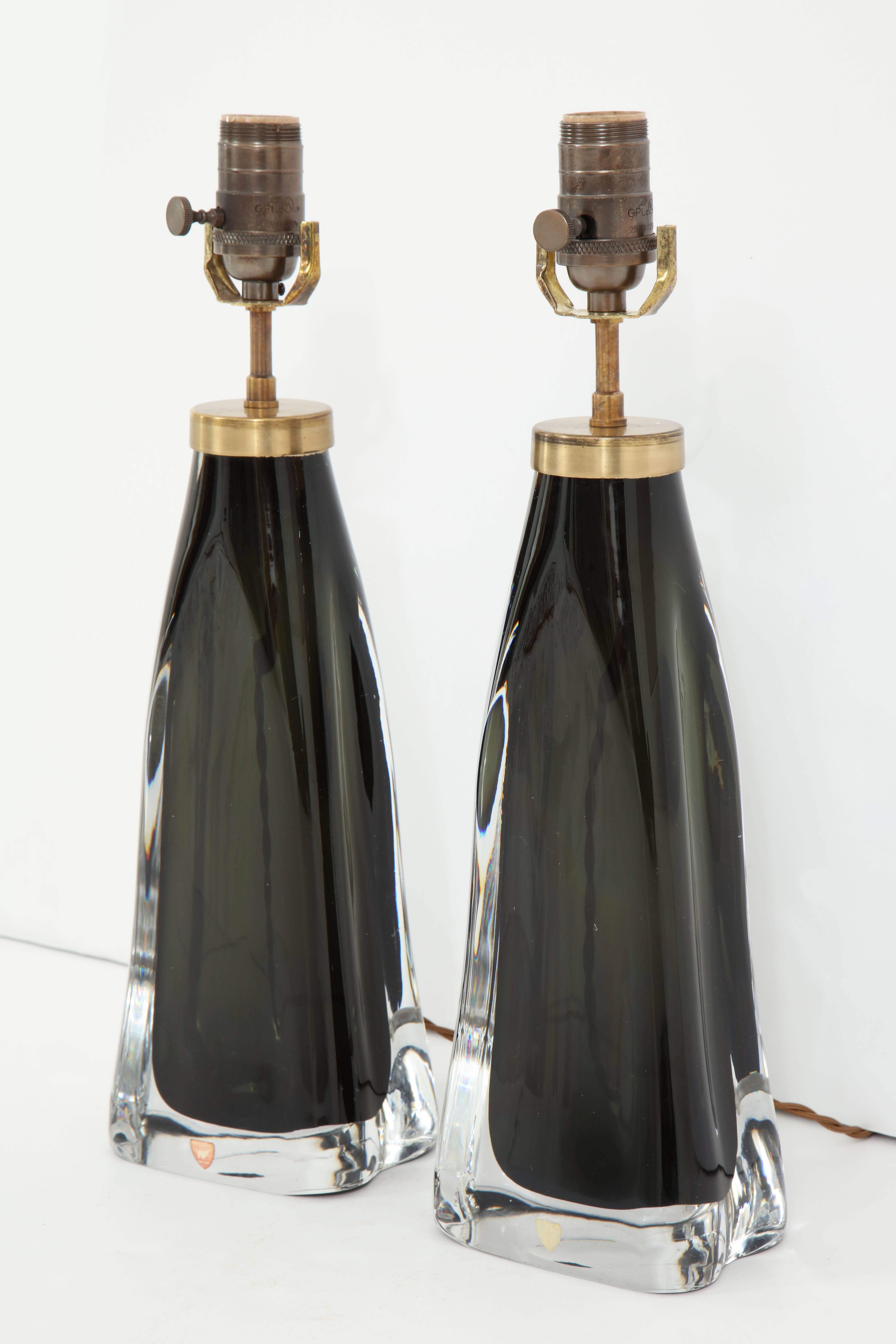 A pair of crystal lamps produced by Orrefors, Sweden, in a stunning midnight blue. The lamps have been recently re-wired for use in the U.S. and have brass fittings with cloth cords. Height listed is to bottom of harp.
