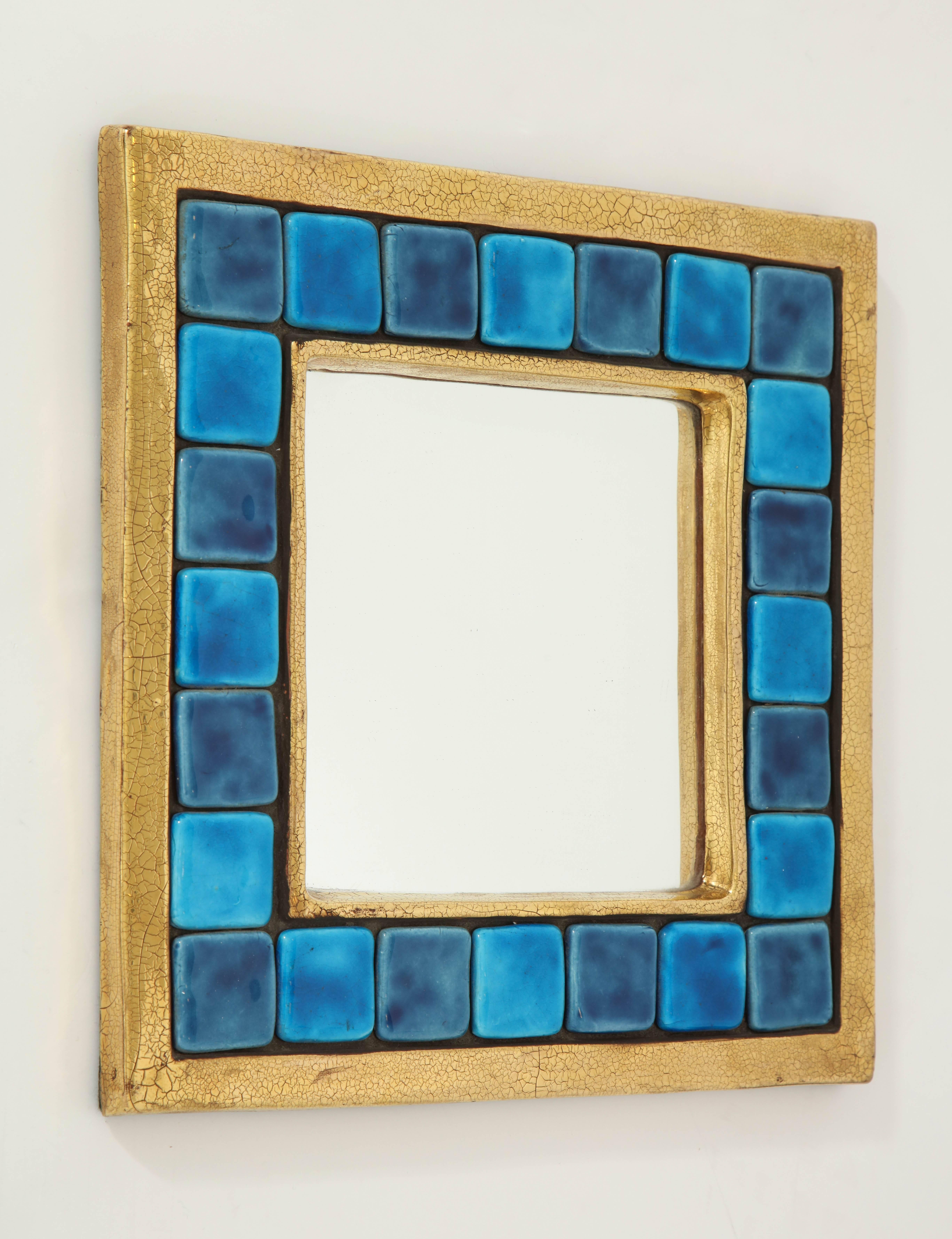 An exquisite work of art created by French designer Mithé Espelt. The ceramic frame features a crackled gold glaze, surrounding square ceramic tiles in various shades of blue. The square mirror is surrounded by an inner gold glazed molding.