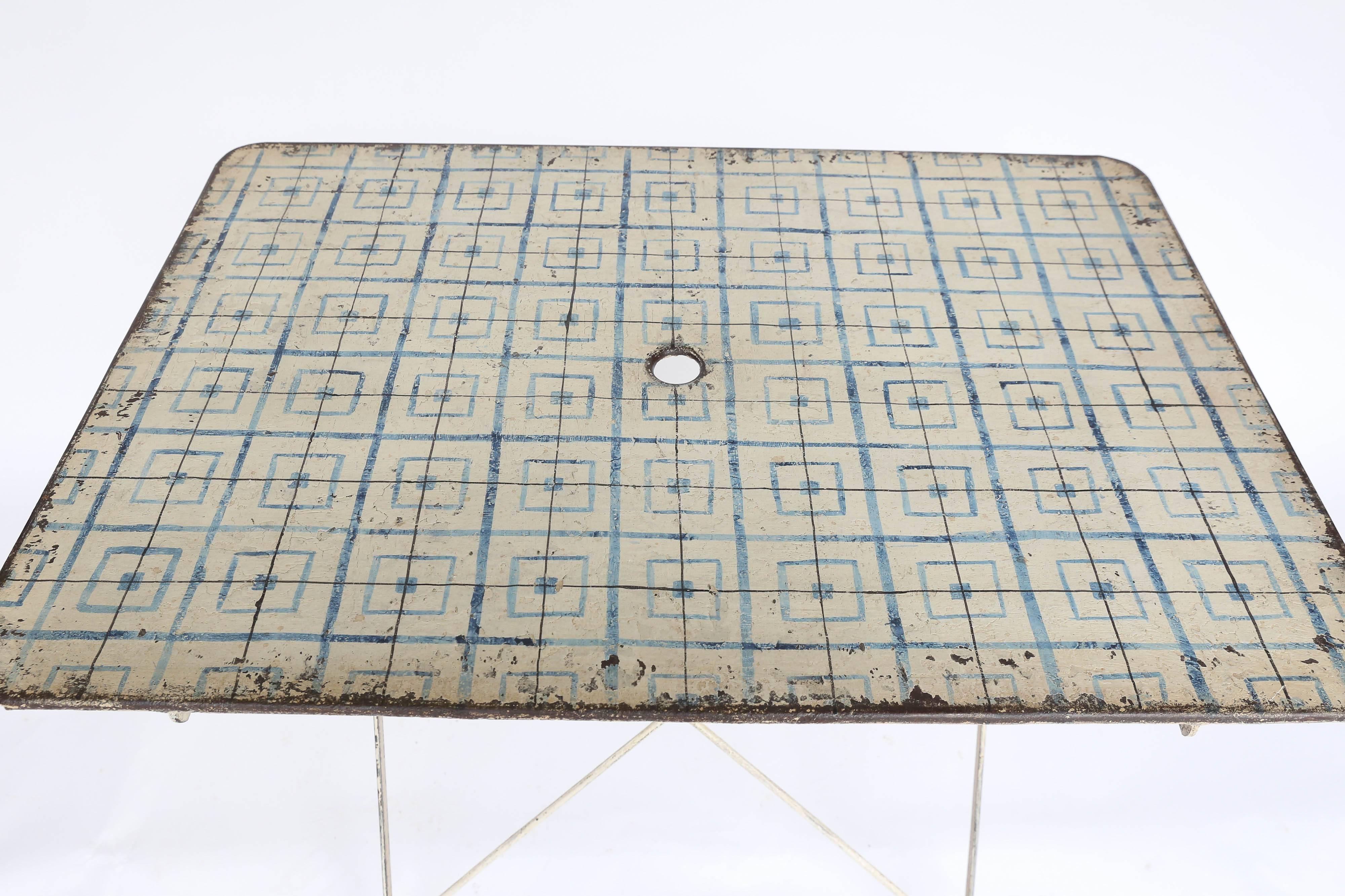 A captivating folding table made of metal found in France. Painted white with a geometric pattern in blue and wear consistent with its age and use, this delightful piece elicits an immediate smile and a sense of a happier time. Still sturdy with