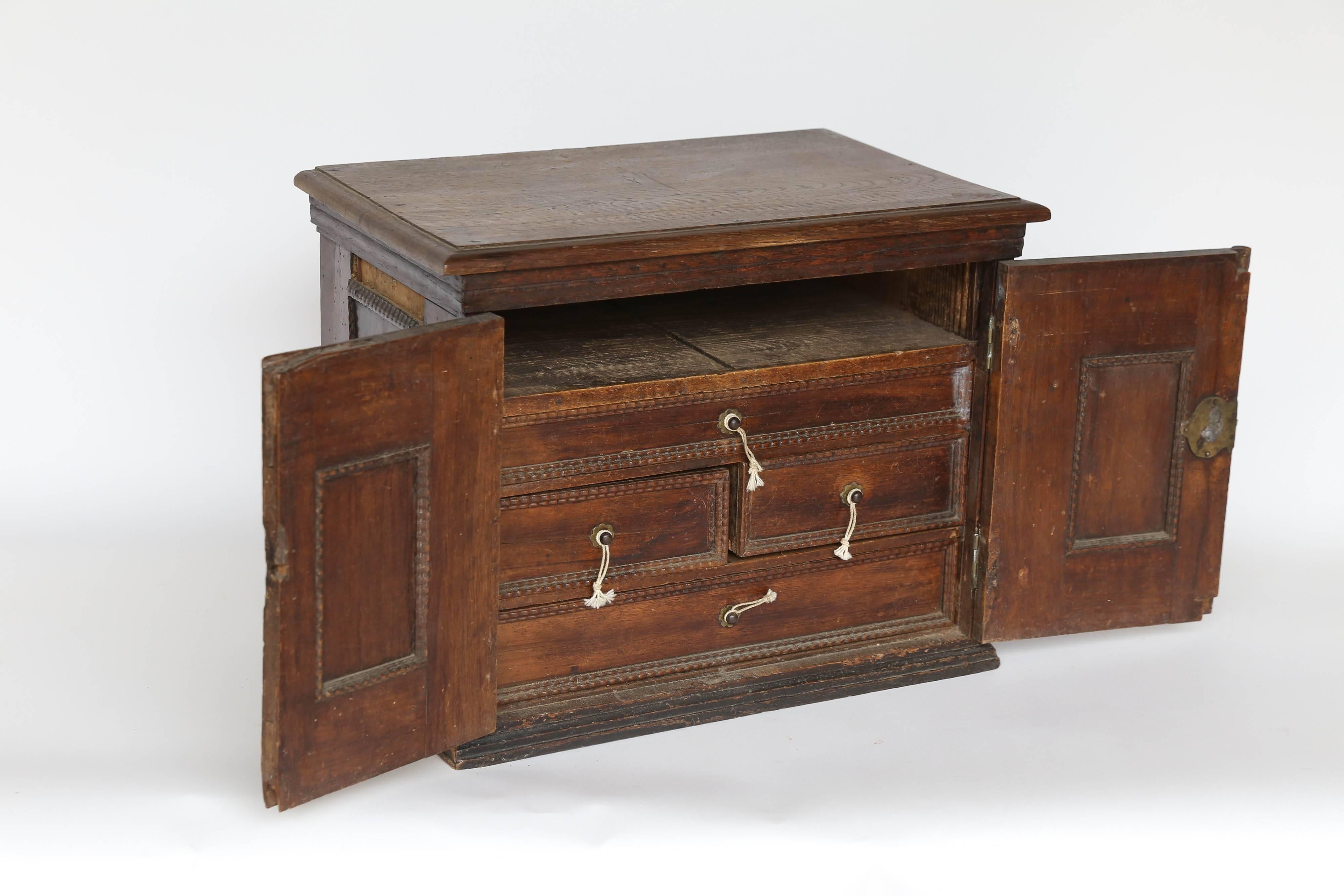 An exquisite antique jewelry box found in France. The carved and paneled doors with ornate escutcheons and hinges open to reveal four drawers and an open upper space. The drawers have tiny brass knobs with woven string pulls. The sides are also