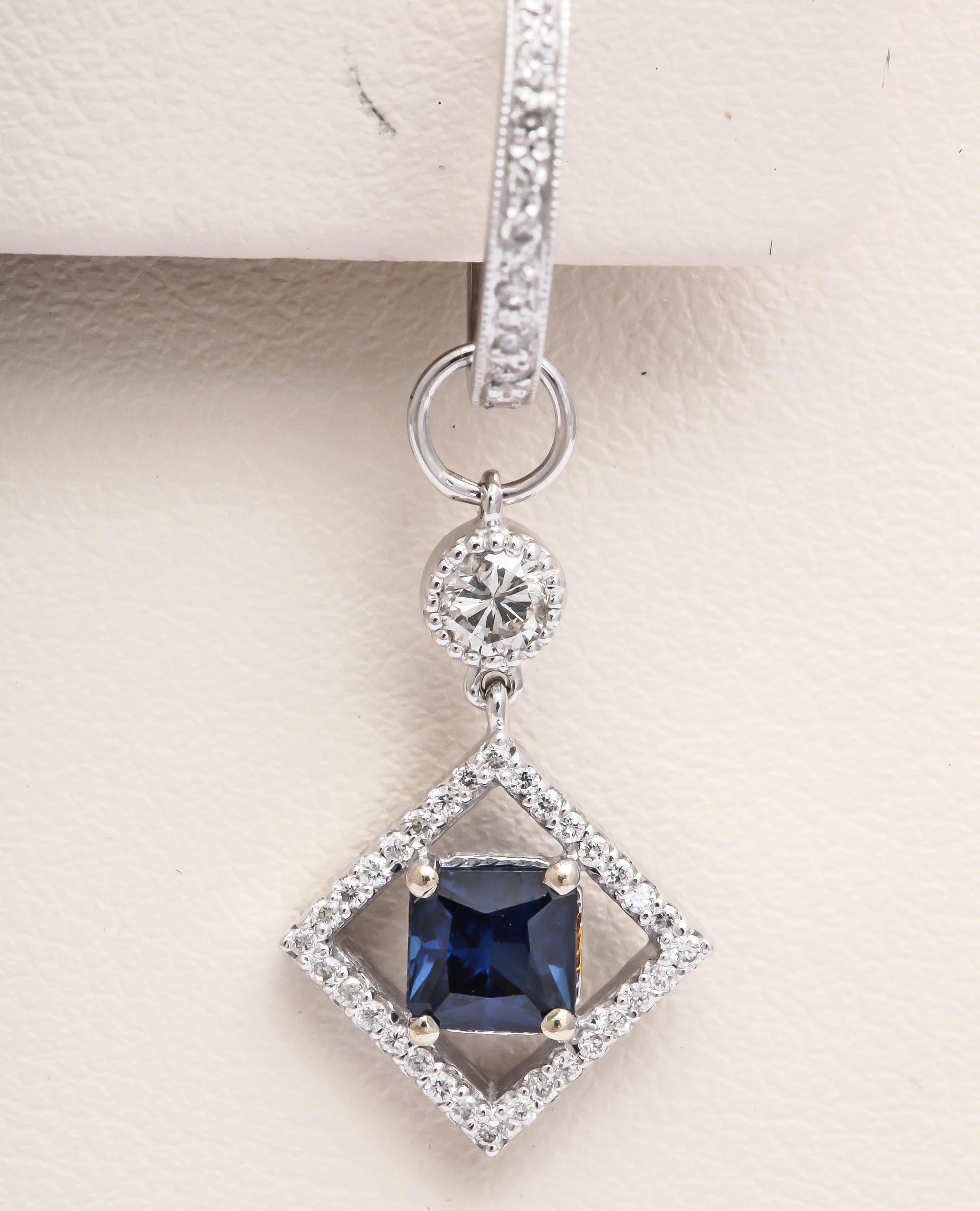 This set of earrings consist of huggies  and a charm. These charms are a micropave set square frame featuring a cushion cut blue sapphire. The charm connects to the huggie with a loop and a bezel set diamond. The huggie can be worn alone. The charms