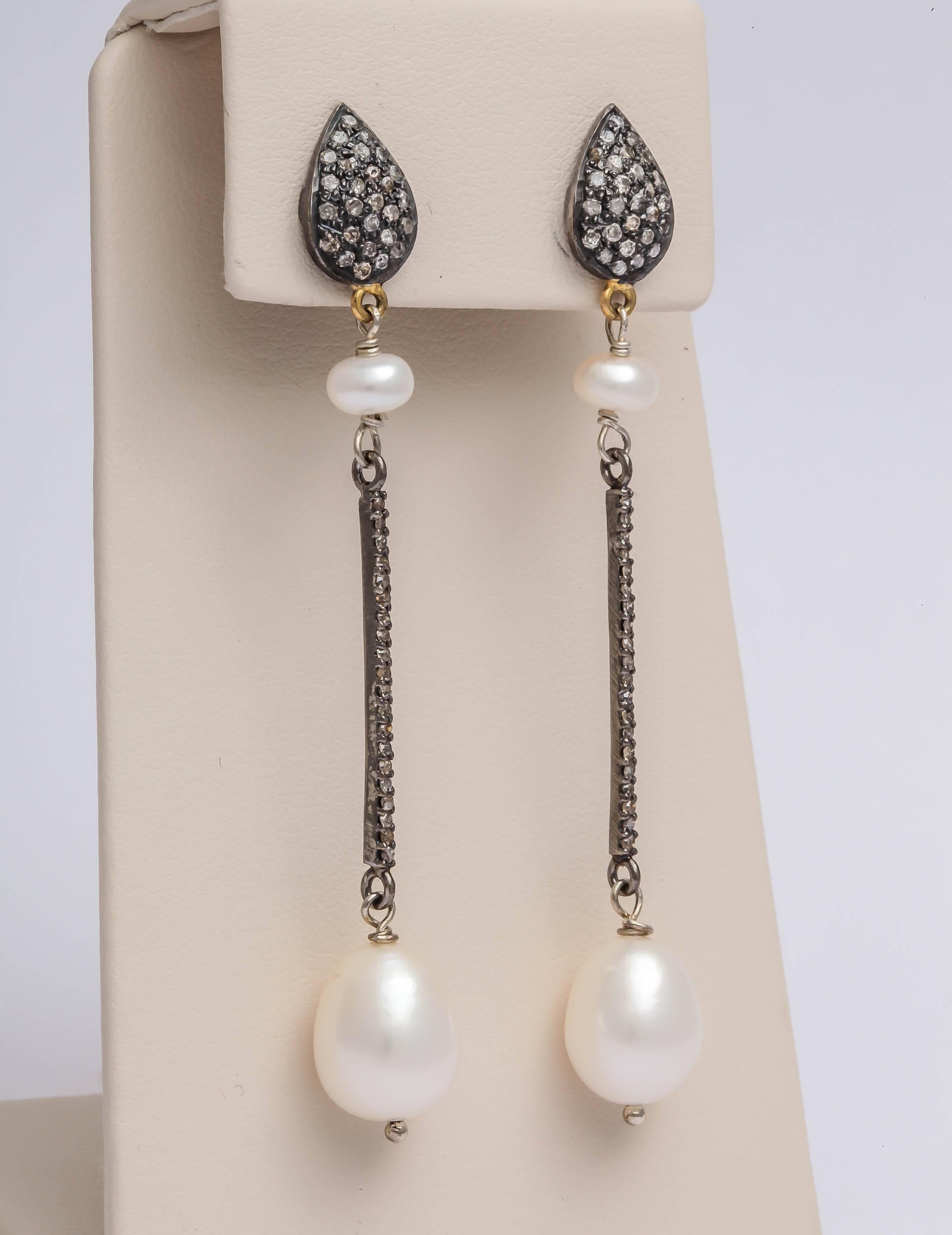 The top of the earring is silver, 14 kt gold and diamonds. It is connected with a pearl that is then connected to a long straight bar of diamonds in silver. The earrings is finished with a 10 x 12 mm fresh water pearl. Flowing and graceful, this
