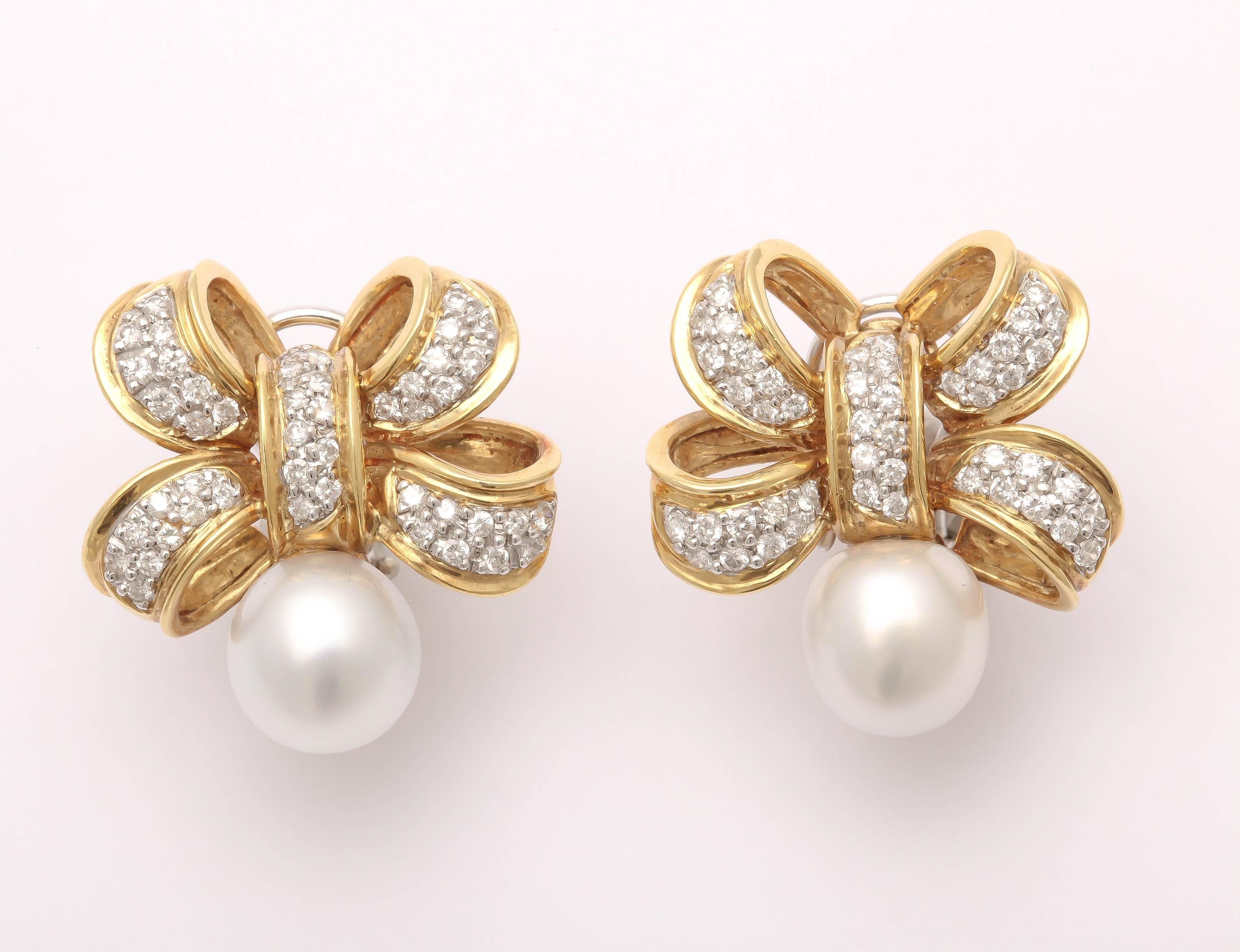 An 18K yellow gold Bow set with pave set white diamonds weighing approx. 0.60ct Tw. Two high lustre 10mm white South Sea pearls finish off the presentation. Omega clip backs,