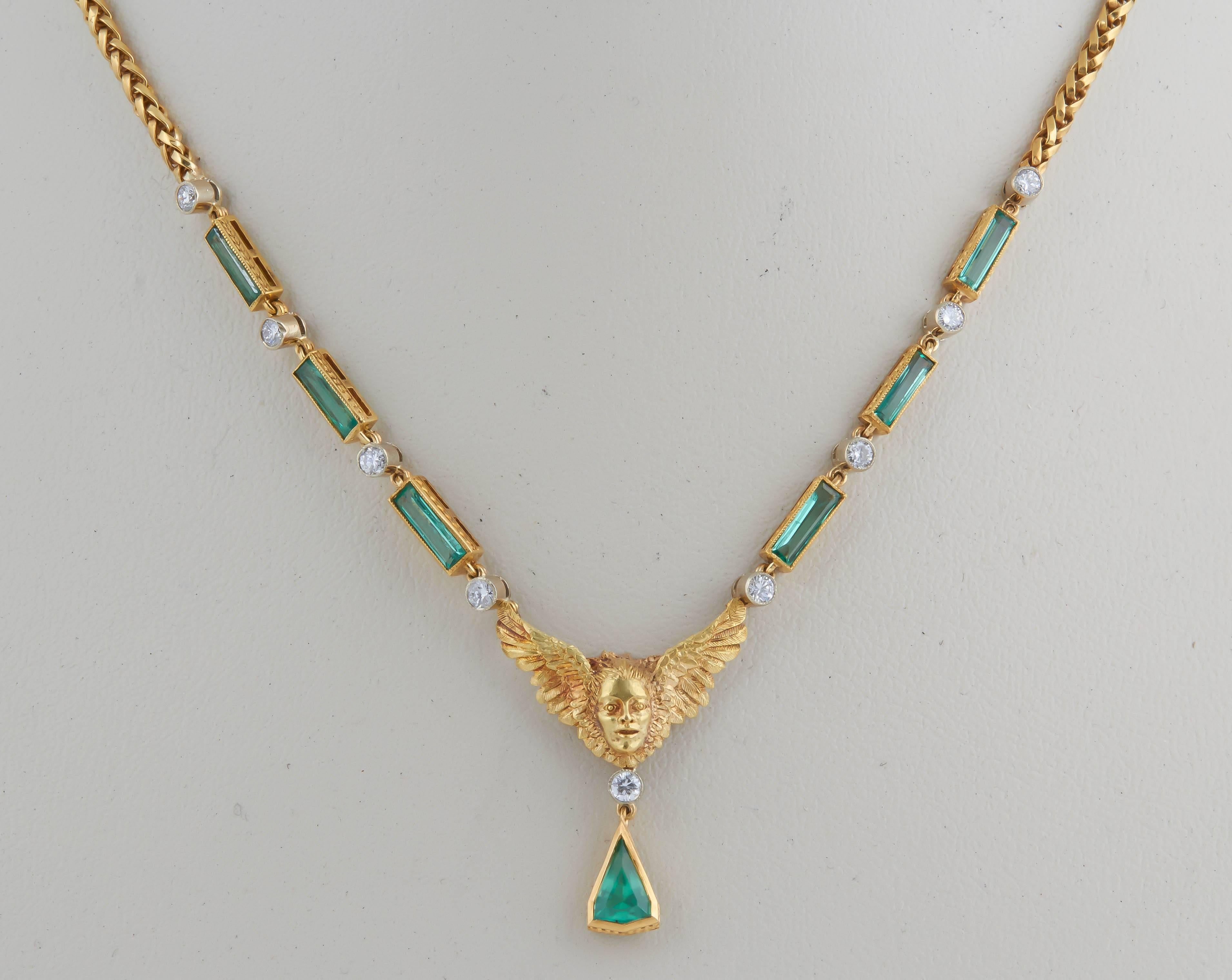 This 18 kt necklace has a cherub face with wings as the central focal point.The emeralds are bezel set, the triangular pendant and the unusually long baguette cut emeralds on either sides of the pendant, are all  delicately engraved as is the