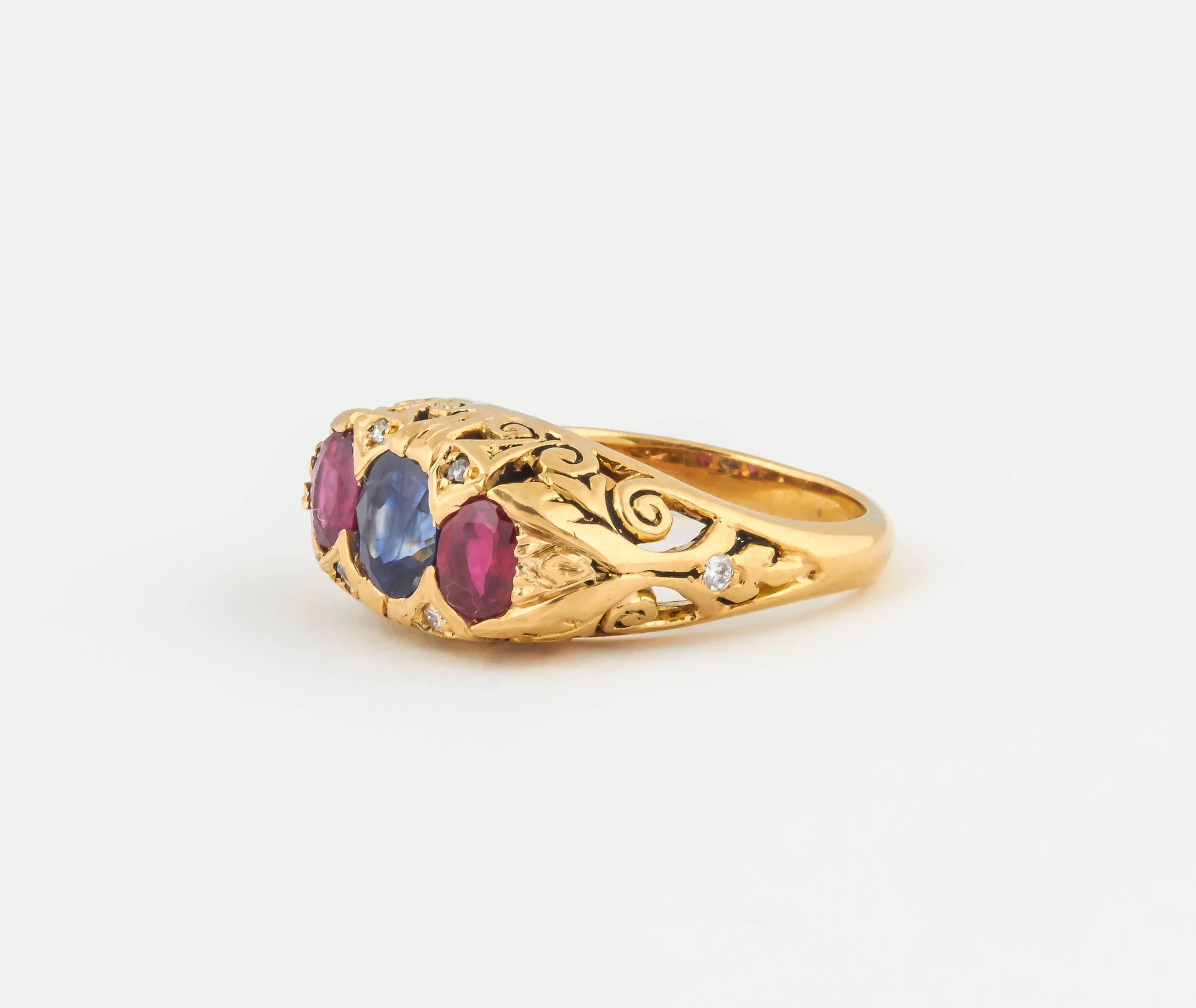 Beautifully carved with a delicate scroll pattern, this ring is set with a  1 ct cushion cut sapphire and 2 oval rubies totaling .80 ct.
The scroll pattern is highlighted with white dismonds all in 18kt gold.The ring is size 6 1/4 and can be sized.