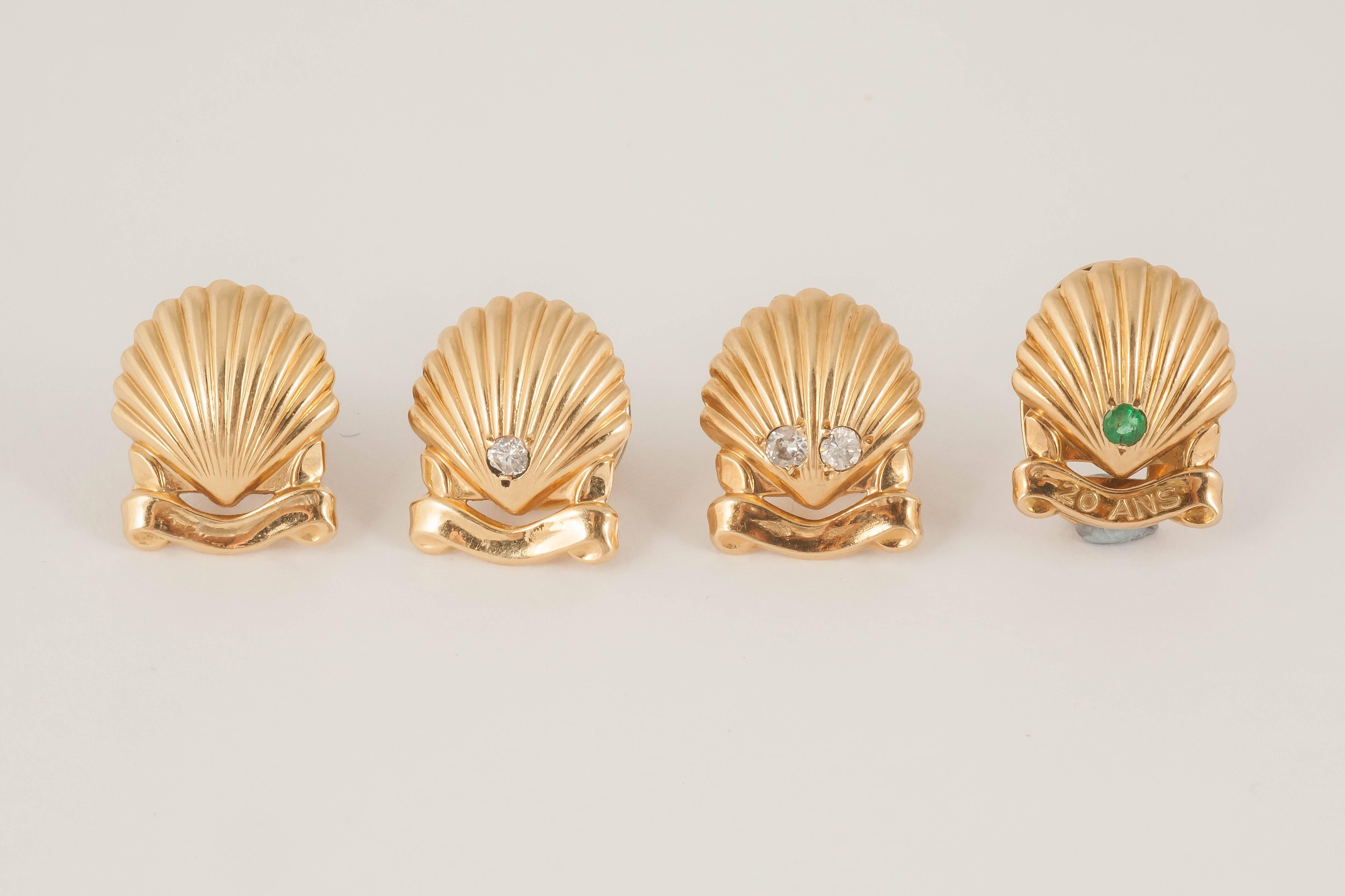 An interesting set of four 18ct gold buttons of shells with cartouche below,one plain,one with one diamond,one with two diamonds,and one with an emerald with 20 ANS engraved below.Signed Cartier Paris with French mark.c,1950