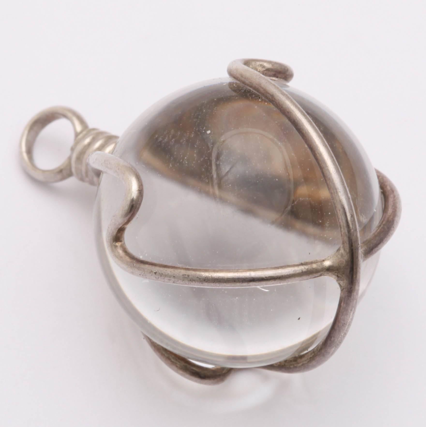 A pool of light emanates from this charm of rock crystal securely wrapped in a cage of silver to be worn at the neck on a chain or added to a bracelet. Around 1900, the Chinese created rock crystal necklaces of various lengths. The orbs were not