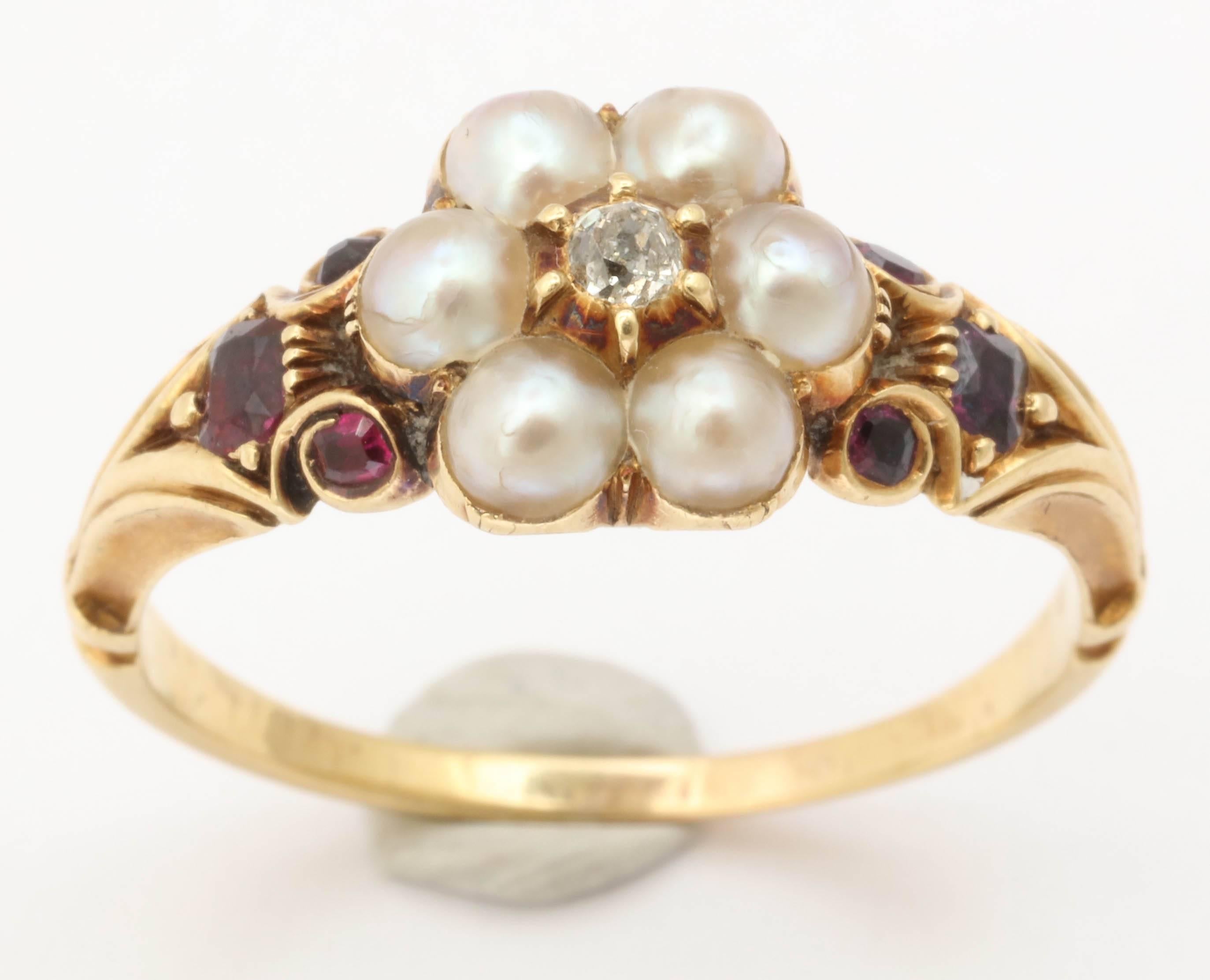 A bit of  Victorian mid summer color loveliness in a 15 kt scrolled shank ring set with the red of garnets, the lovely white of natural pearls, and a dew drop of center diamond . Three garnets rest on each shoulder. The red stones highlight the