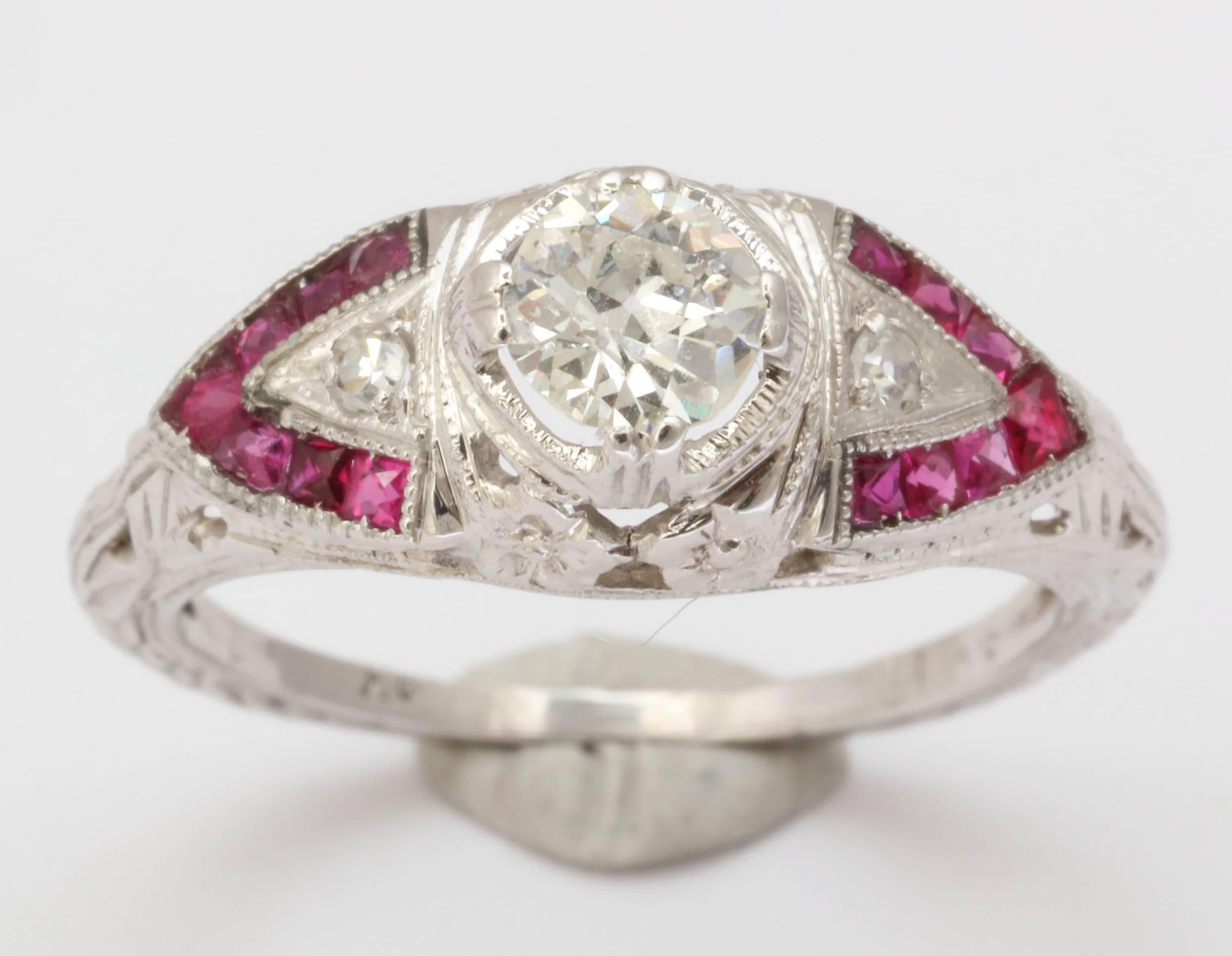Flanked by a chevron of natural rubies a .35 kt Old European cut diamond sits  high, proudly in its 18kt white gold setting. The shank is beautifully engraved in a wheat pattern familiar to the Deco period. The clarity of the diamond is SI. The