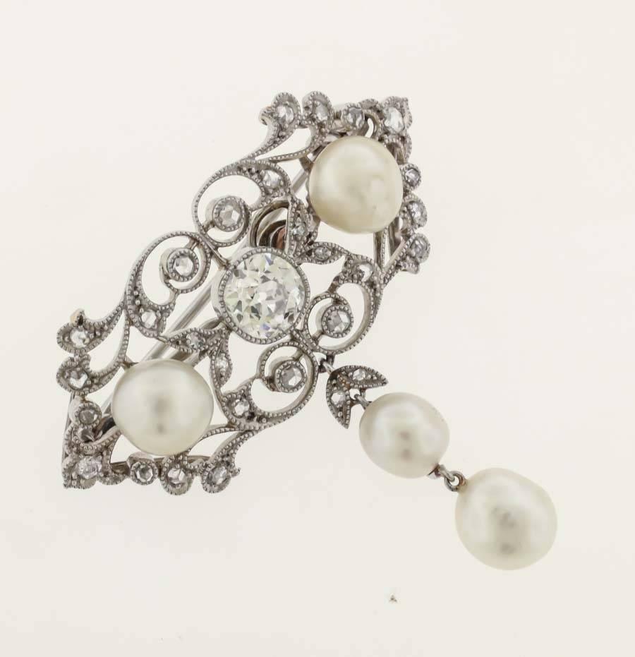 Platinum Edwardian diamond and natural pearl brooch, circa 1918, is set at center with a cushion-cut old European cut diamond, approx. 1.30 cts tw, accented on each side with two natural pearls, and two natural pearl drops., the platinum filigree