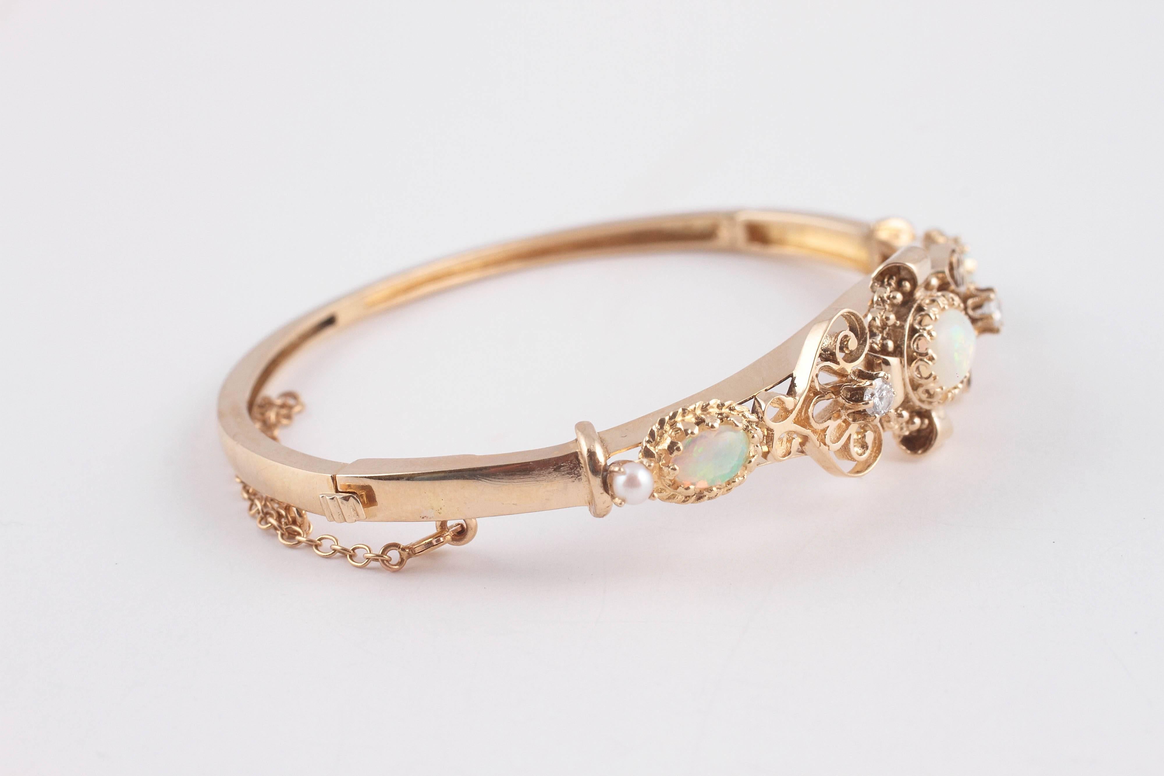 Bright and colorful opals inter spaced with diamonds and pearls in 14 karat yellow gold.  Knife-edge scrolls and broad curls further decorate the bangle with a safety chain to secure the deal.  