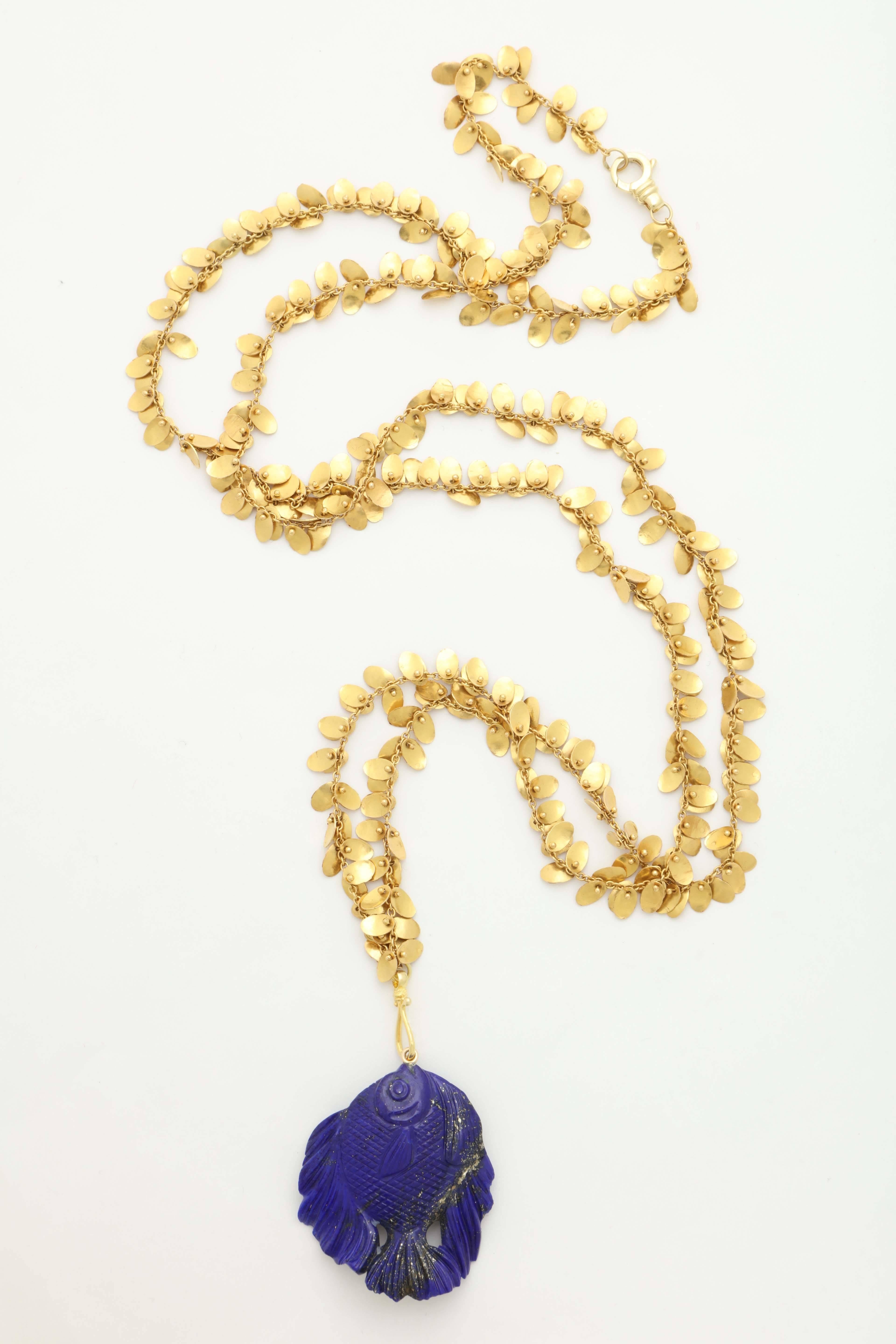 A handmade 18kt yellow gold chain with gold oval discs scattered throughout . There is a lapis lazuli fish pendant suspended from the chain by an 18kt yellow gold hook. The fish was carved in Idar Oberstein.
Length: 42 inches
Length of fish: 1.70