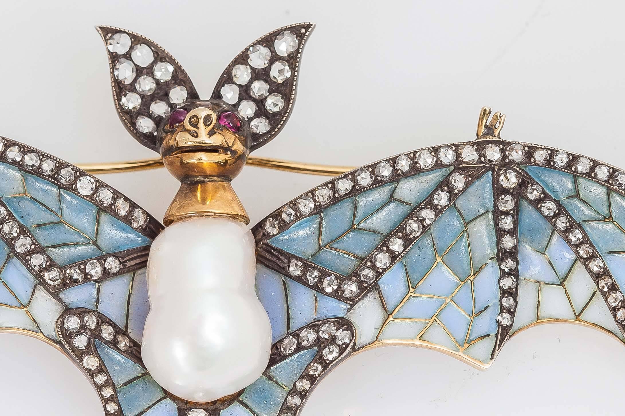Beautiful bat brooch finely crafted in 18k yellow gold and silver with light blue plique a' jour wings and round brilliant cut diamonds weighing approx. 2.00 carats and baroque pearl body and ruby ayes. 