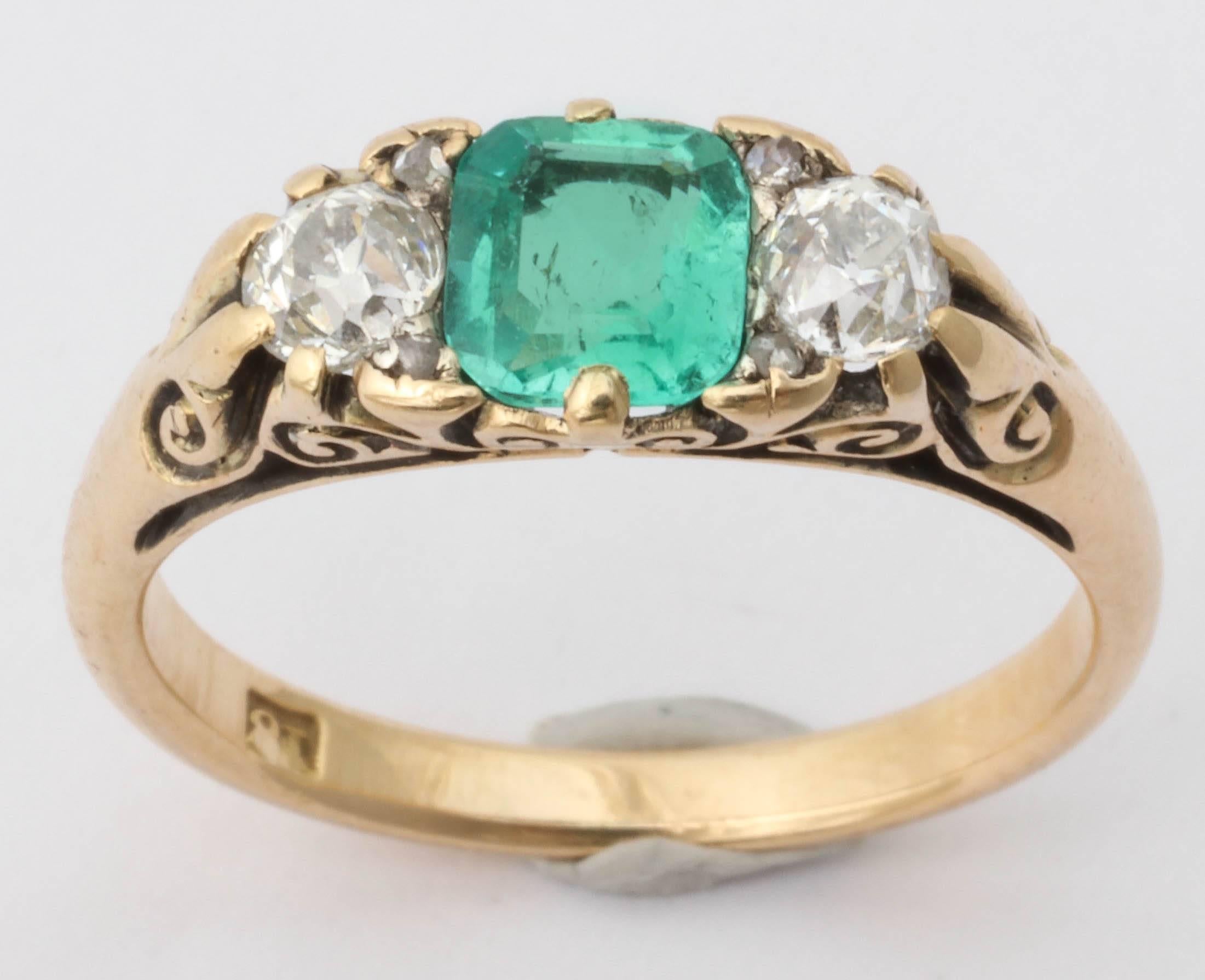 A lovely Victorian ring in 18K yellow gold set with a central emerald. The emerald is lighter in color without heavy inclusions visible to the naked eye. Two rose cut diamonds and an old mine cut diamond flank either side of the emerald. Approximate