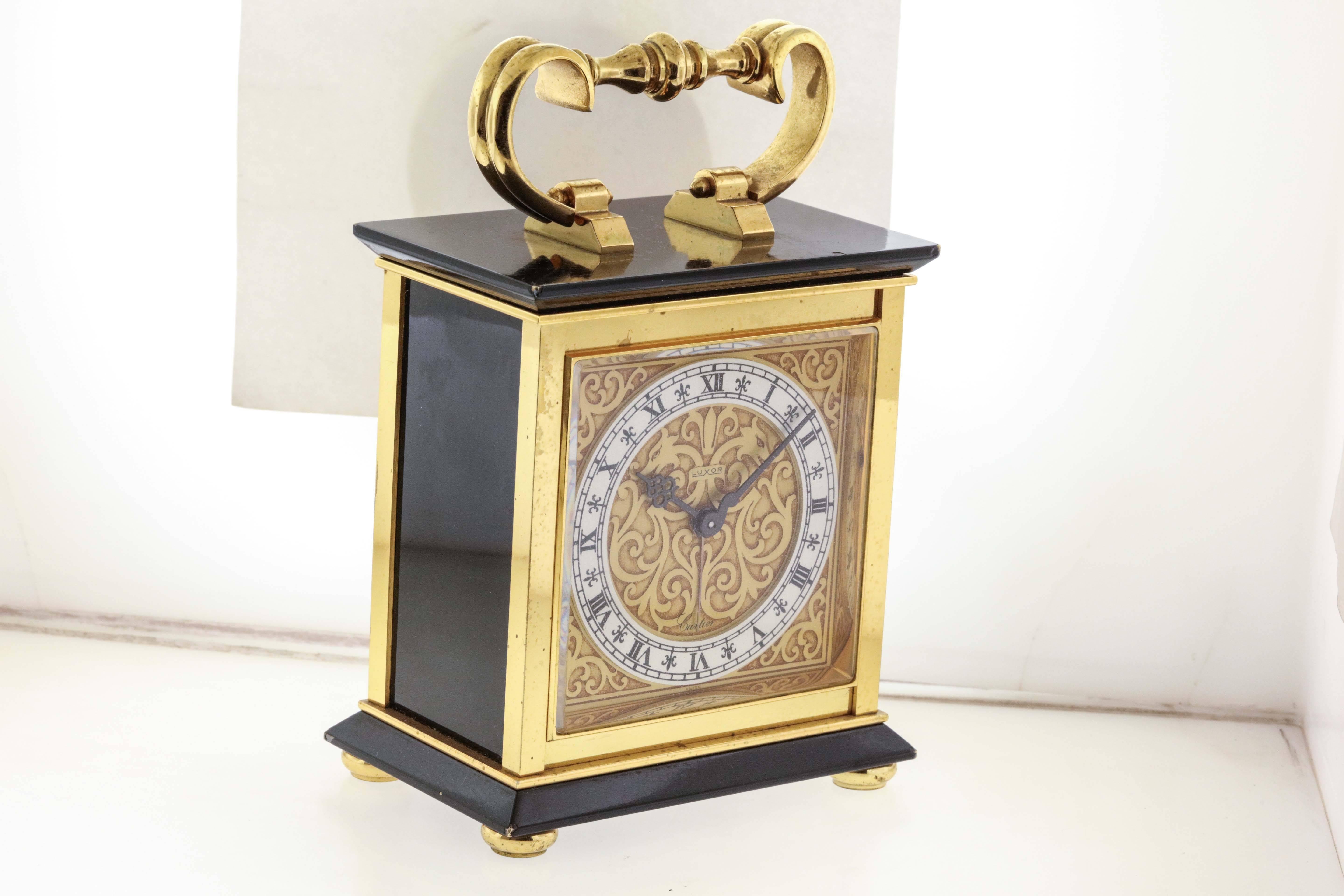 Cartier desk alarm clock, the movement by Luxor, Swiss, made circa 1960's, is a gilt-brass and painted 8-day going desk clock with alarm and decorative Louis XV style brass handle.  The 3-1/4