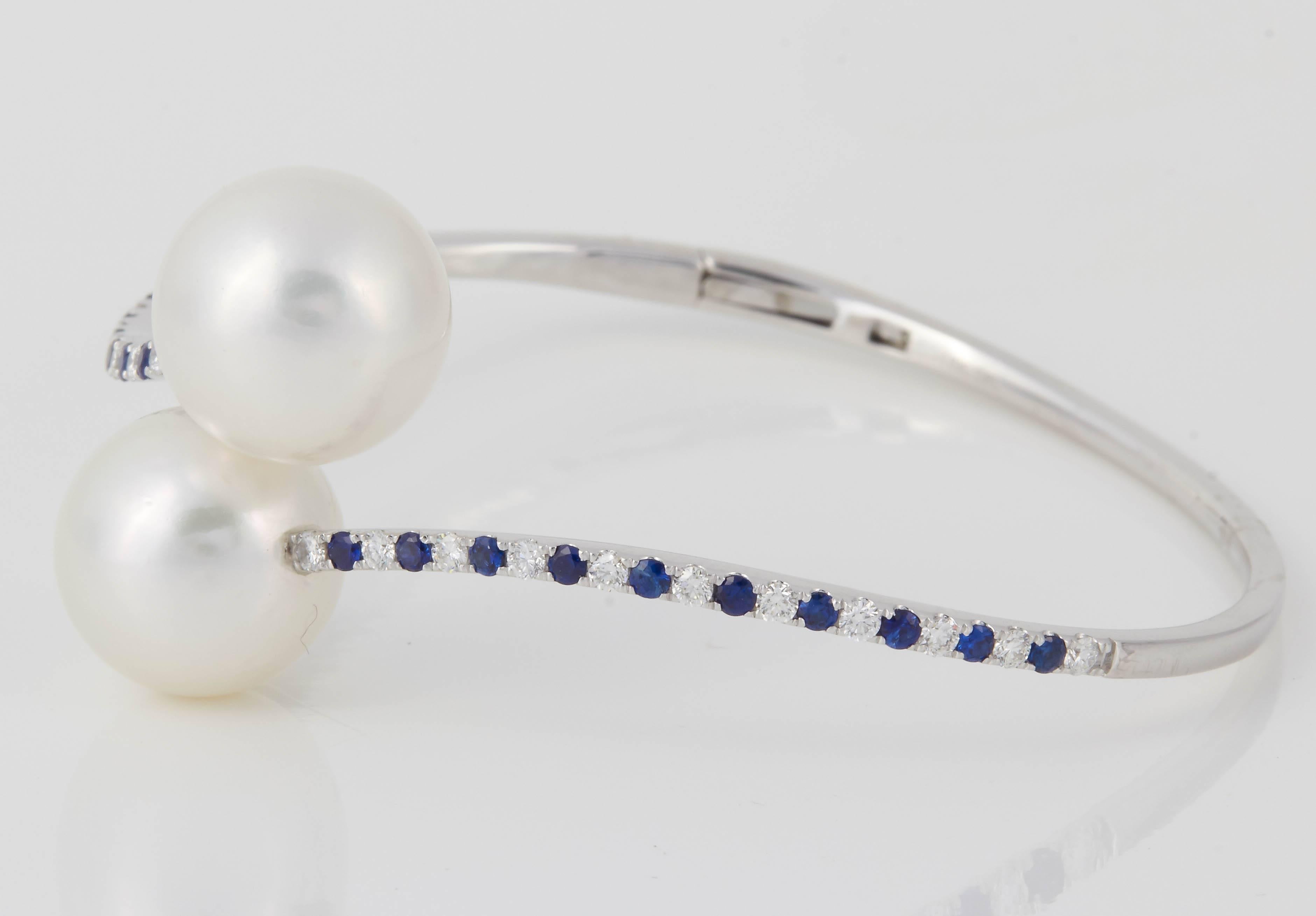 18K White gold bypass bangle bracelet featuring two South Sea Pearls measuring 13 mm flanked with sapphires weighing 0.55 carats and diamonds weighing 0.55 carats.
8.5 Grams
Color G-H
Clarity SI

Pearls can be changed to Pink, Tahitian or Golden
