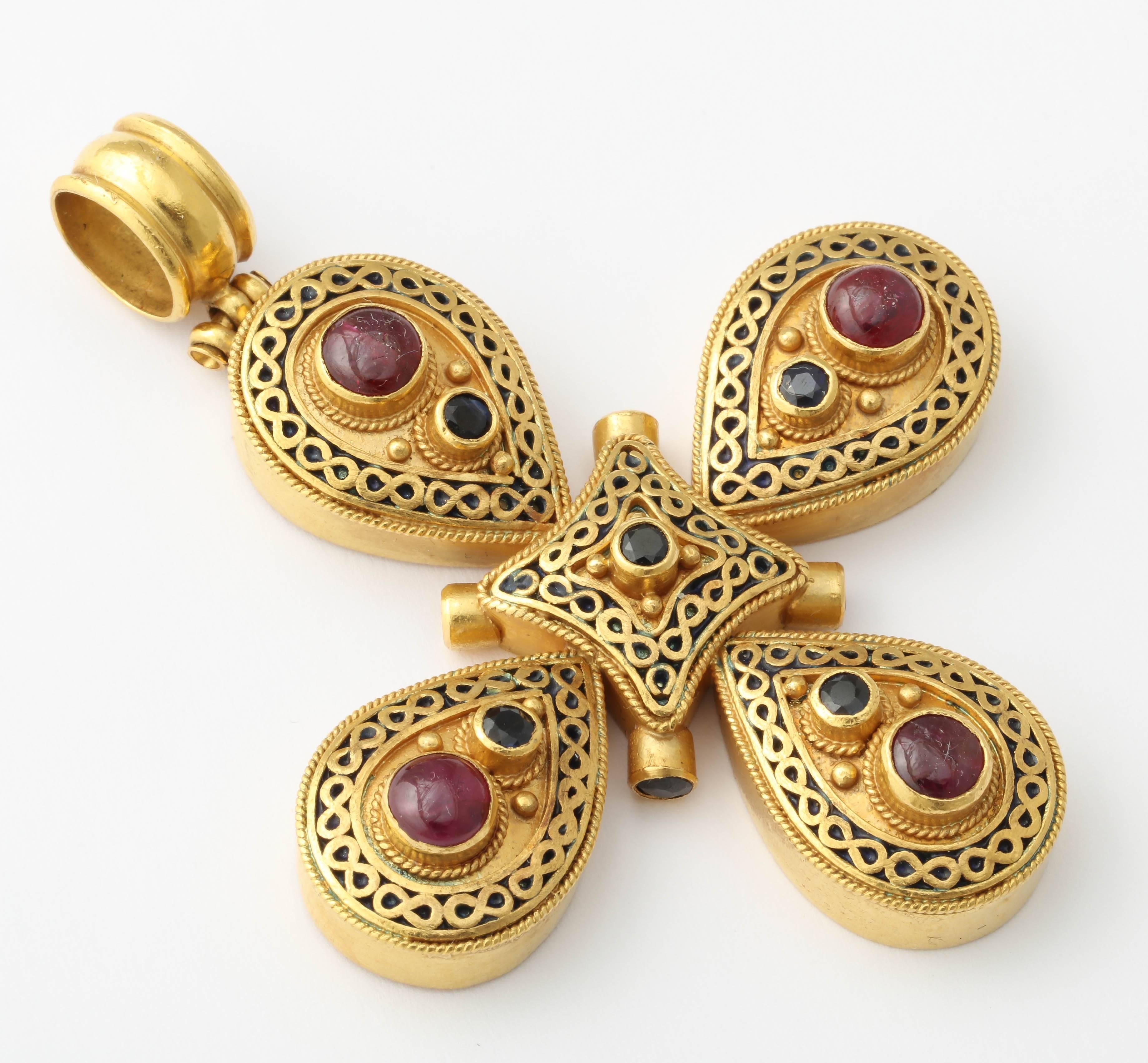 22kt Yellow Gold Cross in Medieval Style and set with4 Cabochon Rubies, 9 faceted Sapphires with Black enamel set between stylized figure 8s.  Marked T35 no. 91.8 to indicate 22kt.  Very Rih and definitely a Cross - yet still stylized enough to