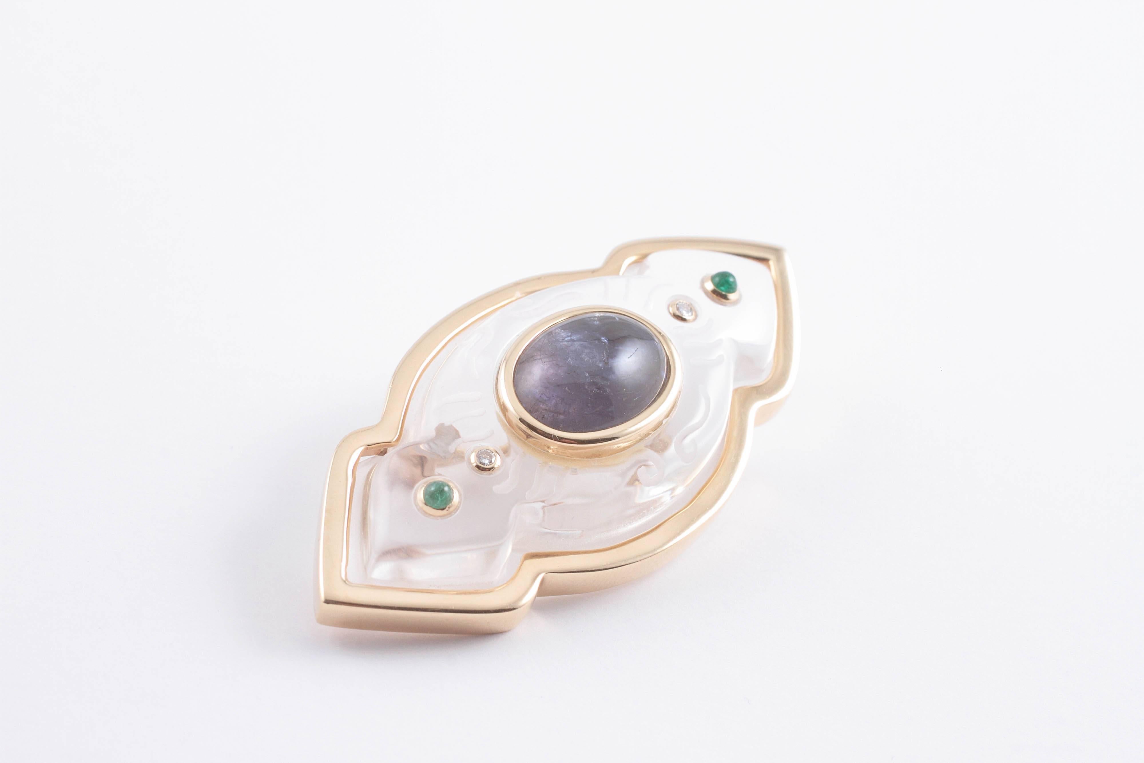 Colorless and frosted crystal centered with a cabochon cut blue sapphire accented with emeralds and diamonds all framed in yellow gold.  Designed and created by Trianon. 
