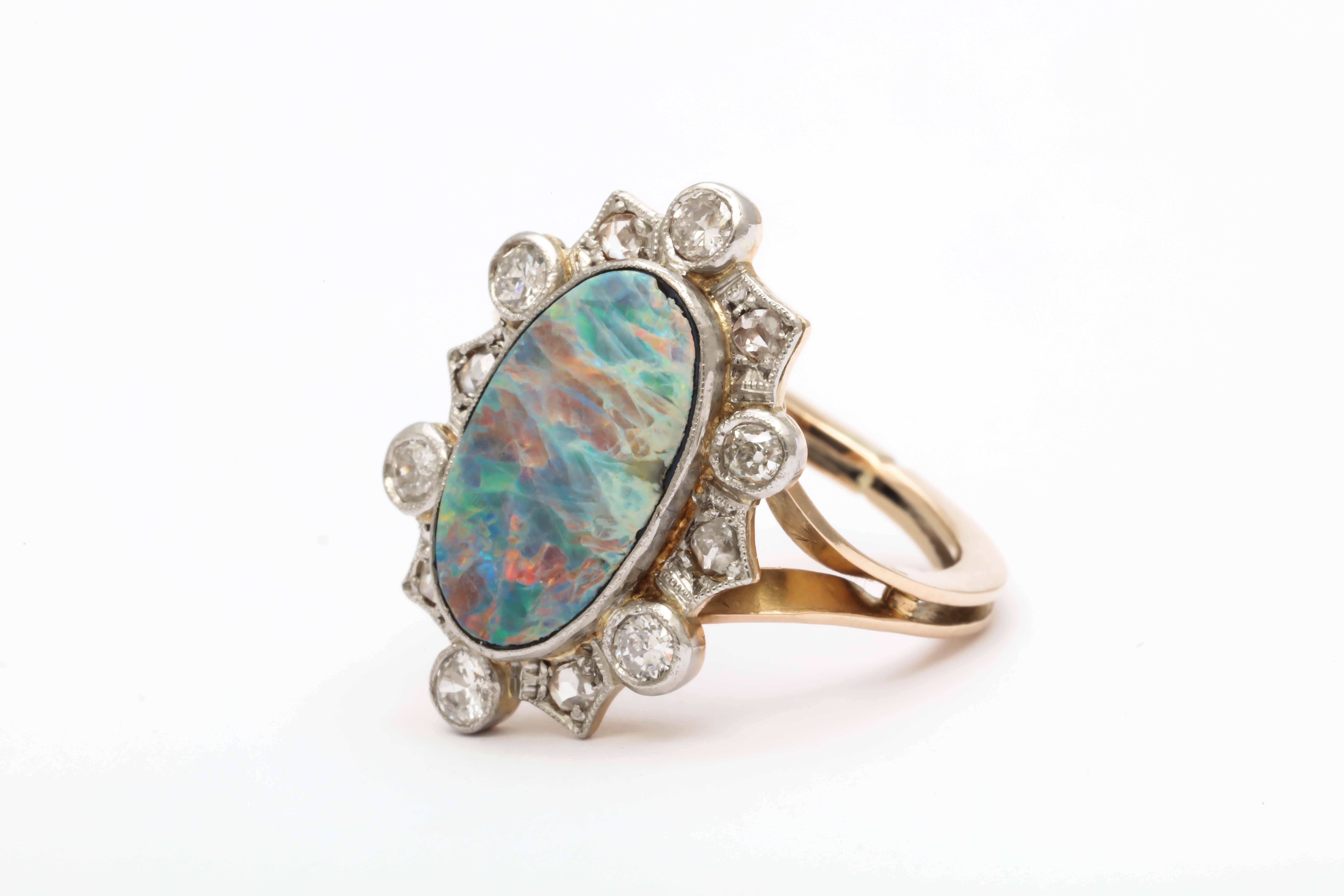 Full of sparkle, this early 20th century opal and diamond ring is platinum on 18K yellow gold. The opal is surrounded by 12 old cut diamonds. It was originally a brooch and made into a ring by wrapping the bar section from its horizontal origins