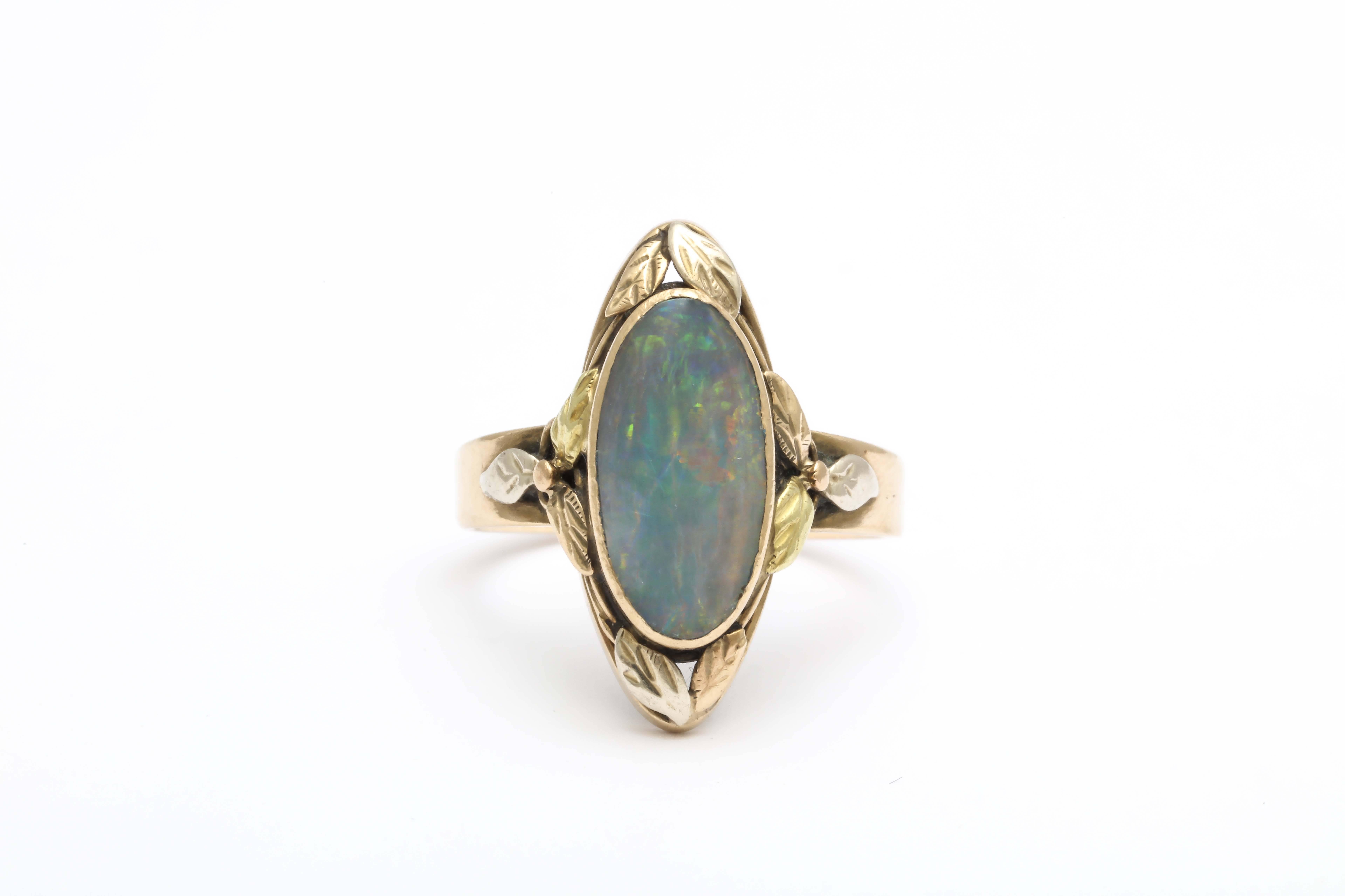 A 10K American made Arts & Crafts ring. An oval opal is set surrounded by leaves of white, yellow, and pink gold. This anti-industrial movement was meant to take artists back to their roots. Forms were simple and the idea of the handmade in both