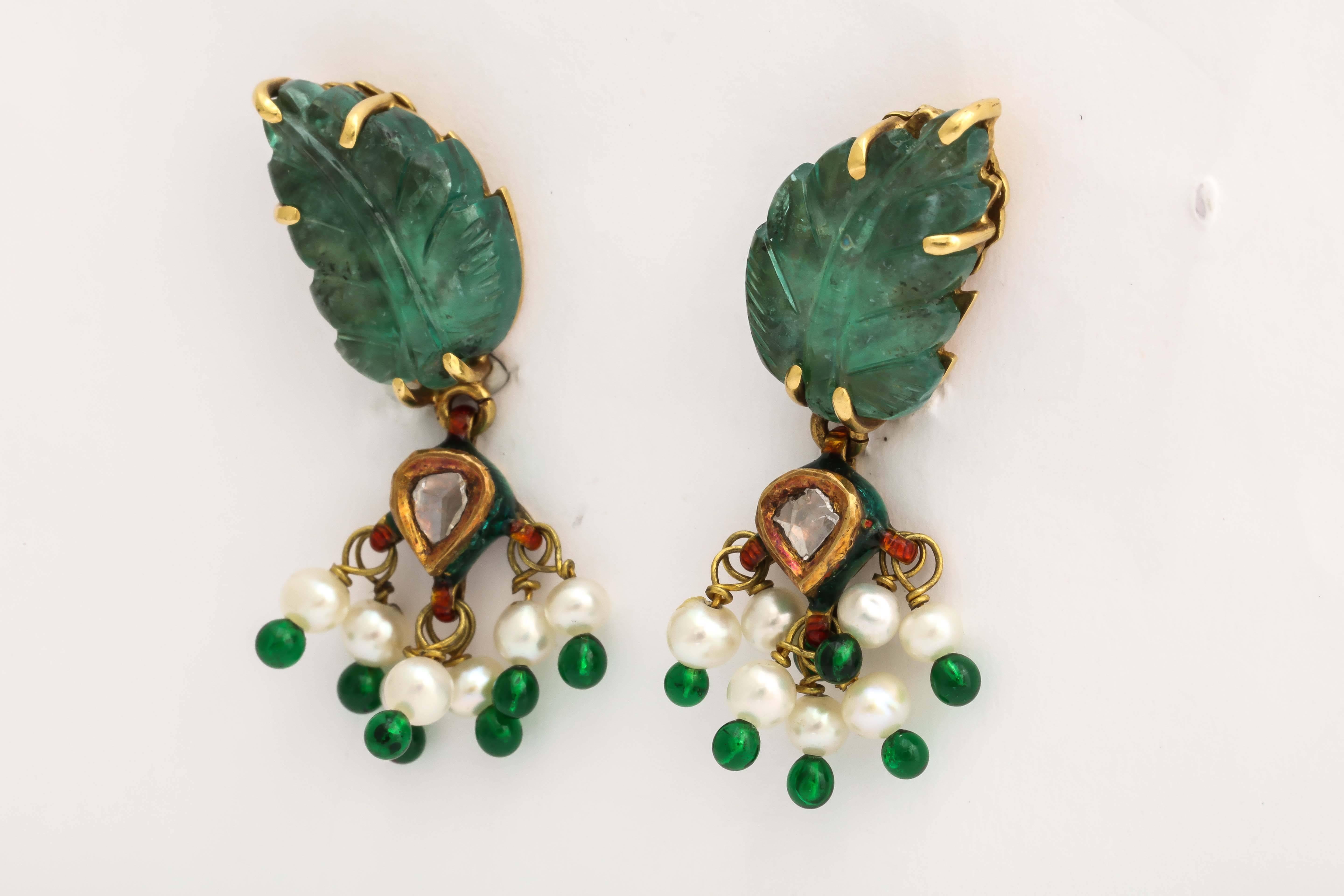 These beautiful emeralds were carved into leaf shapes by the skilled craftsmen in India. They are custom set in 18 kt yellow gold with an Indian polki diamond in the center and pearls tipped enamel clusters dangling from the emerald settings.
The