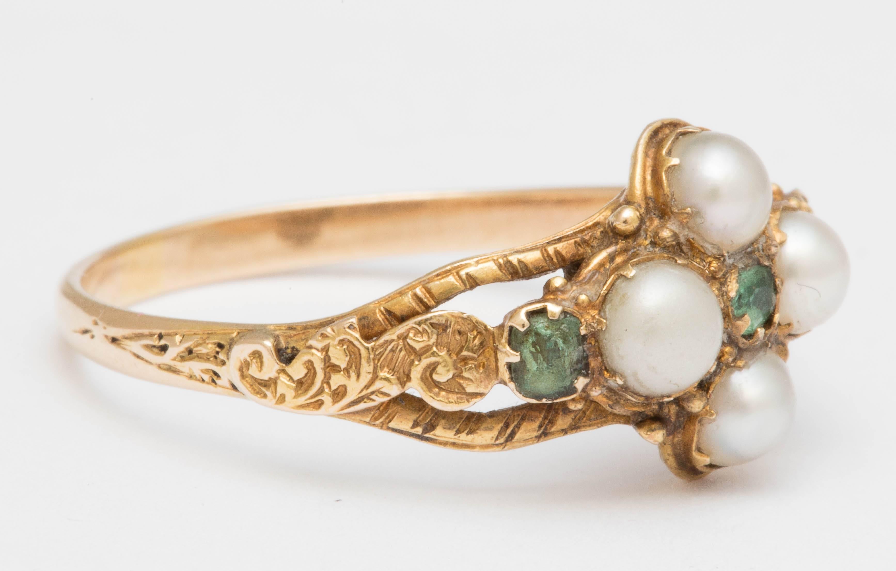 Mid Victorian 15K pearl cluster ring set with a central emerald. One emerald is set in each shoulder. Lovely engraving on the top and shoulders of the ring. Underneath is a locket compartment. 