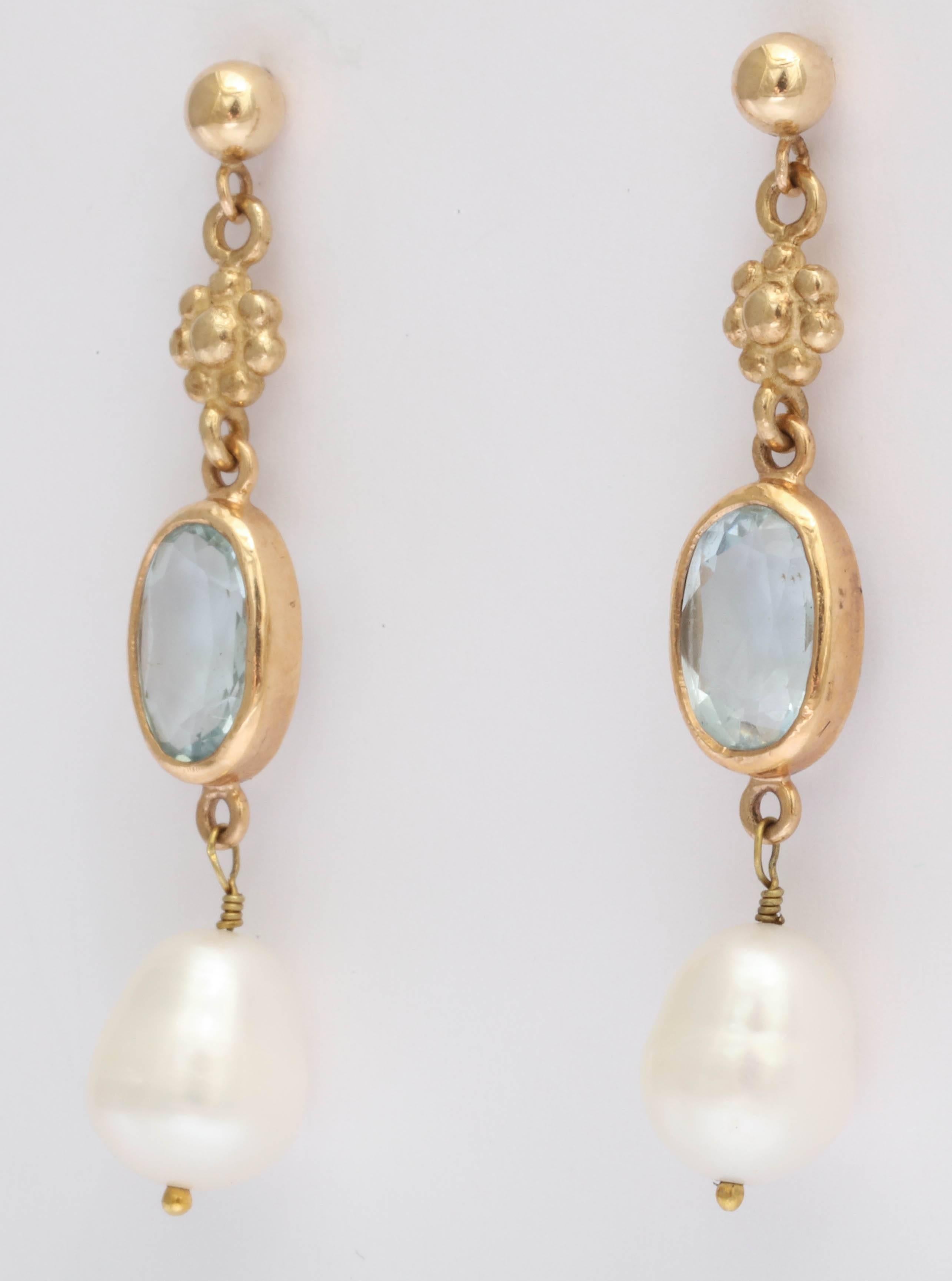 The oval aquamarines are a beautiful blue. They are faceted and  7 X 12 mm, set in a 14 kt gold bezel setting. The earring has a ball and post top with a gold rosette connecting the aquamarine. Off the end of the earring hangs  a pear shape fresh