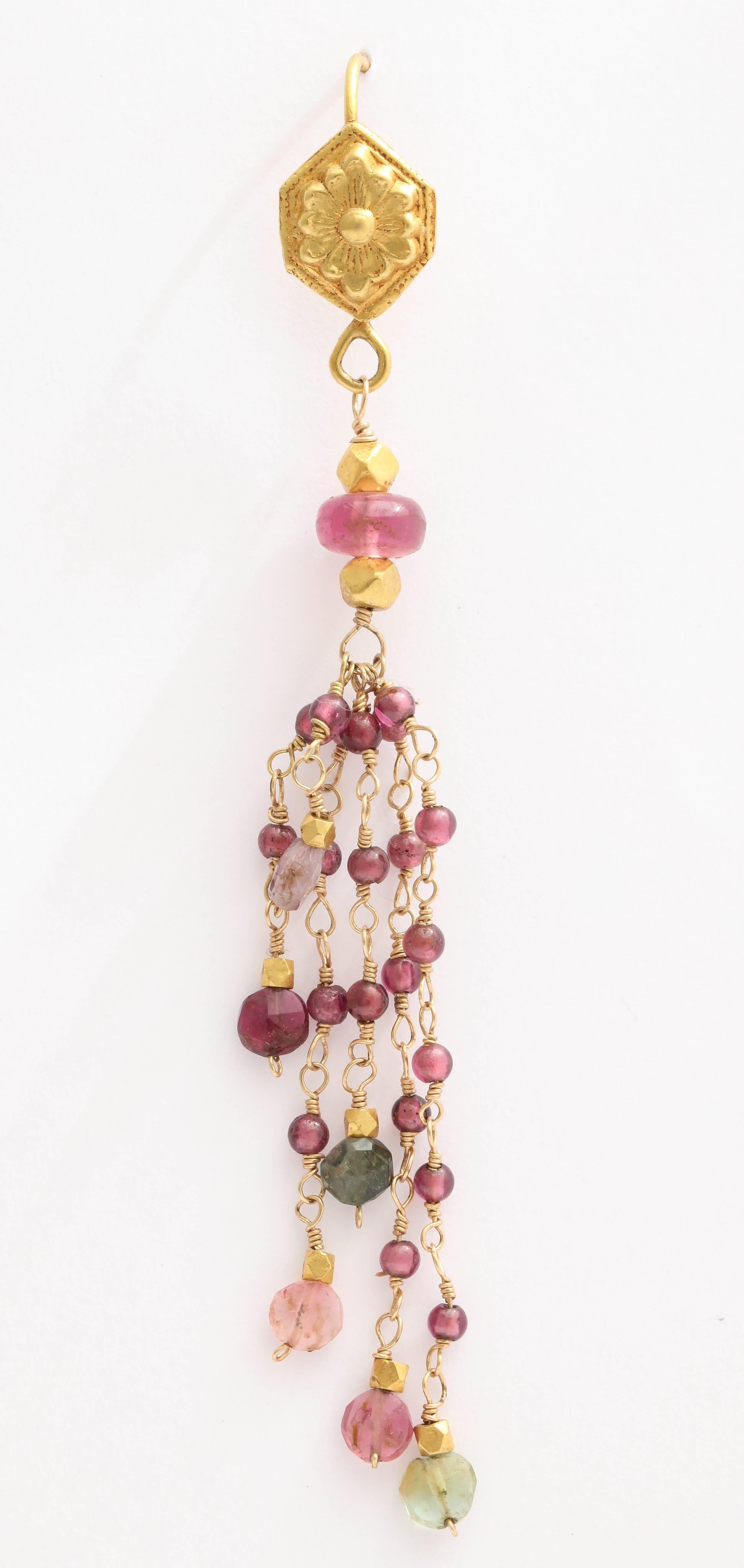 Each chain has hand wired  2 mm garnet beads with a faceted tourmaline bead at the end. The top of the earrings is a hand hammered floral design connected to the ear wire.  The beads are also interspersed with 18 kt gold faceted beads. The earrings