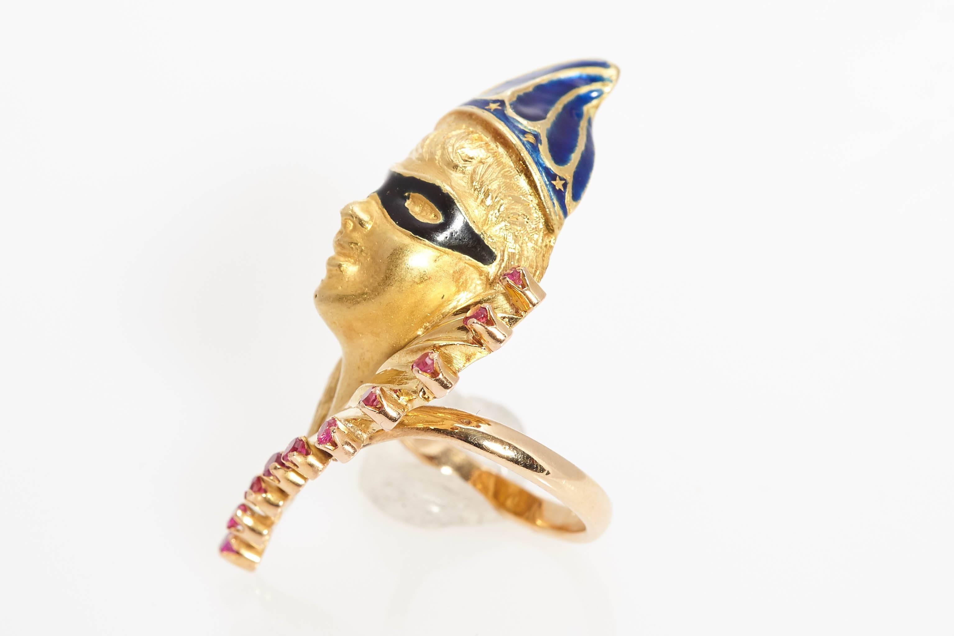 A peculiar Venetian Mask ring, representing Arlequin, in 18kt yellow gold, rubies and blue and black enamel. Made in Italy, circa 1970. 