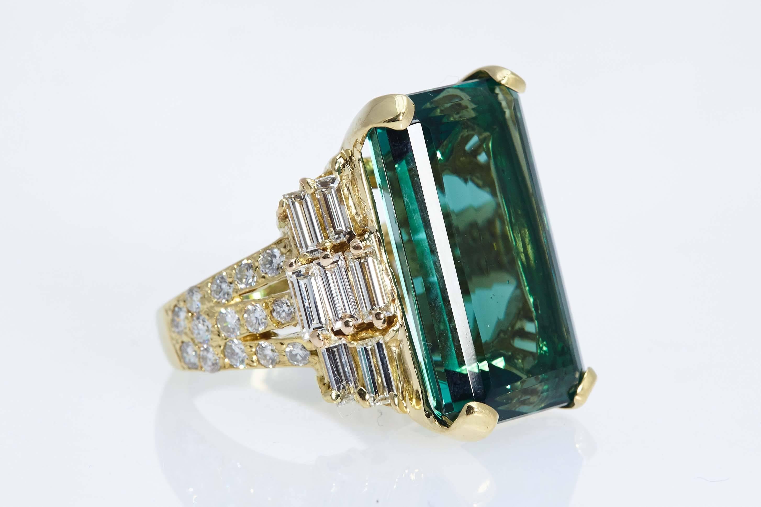 Emerald cut Tourmaline ring in eighteen karat yellow gold with diamonds on the sides. The tourmaline weighs 22.98 carats and the ring contains 14 straight baguette shaped diamonds weighing 1.91 carats and 28 round diamonds weighing 1.01 carats. The