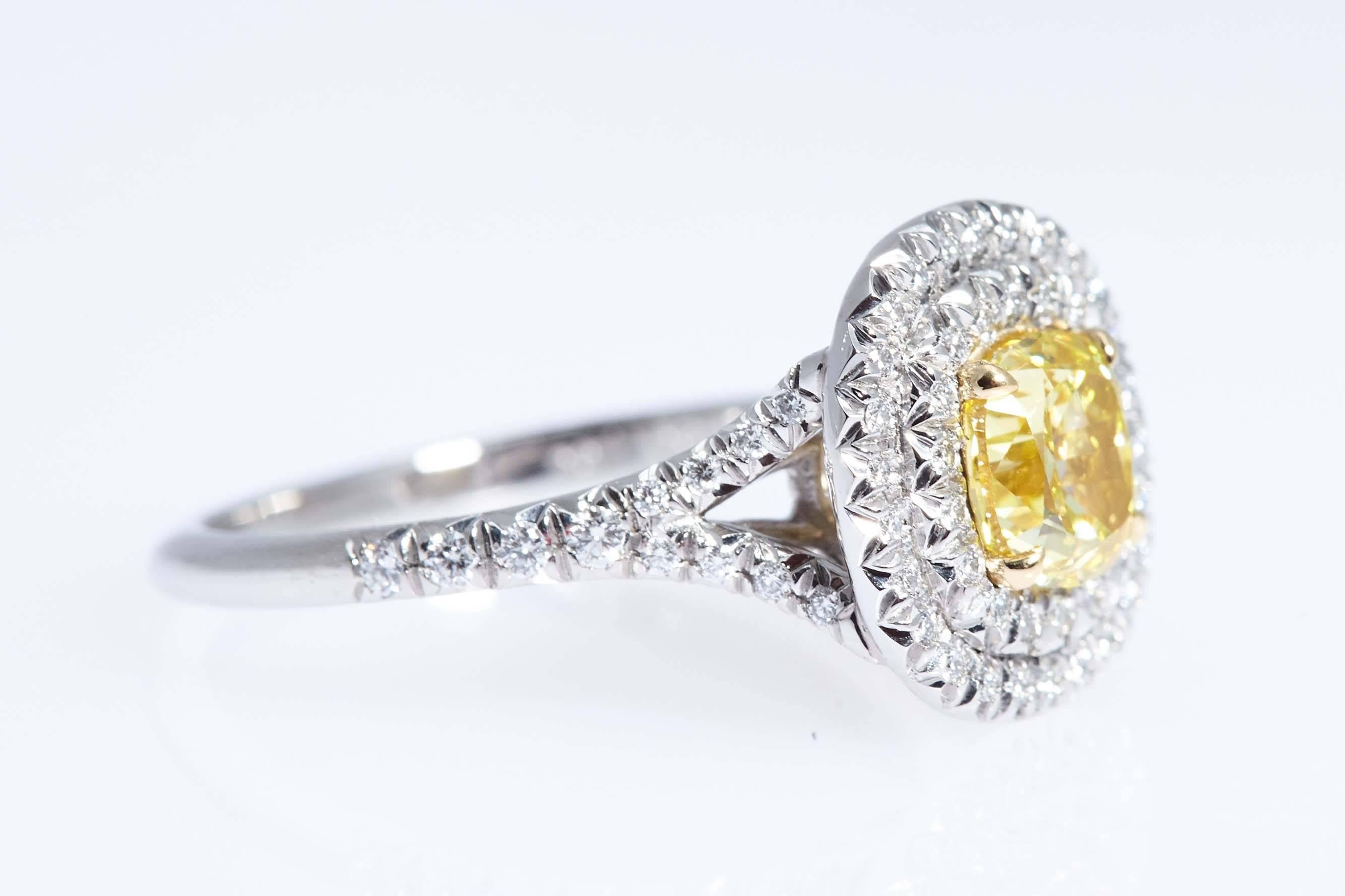 GIA graded Fancy Vivid Yellow Color and "SI1" clarity 1.04 carats cushion shaped diamond. The diamond is set in a custom made platinum and 18 karat yellow gold ring with two rows of diamonds encircling the cushion shaped diamond and