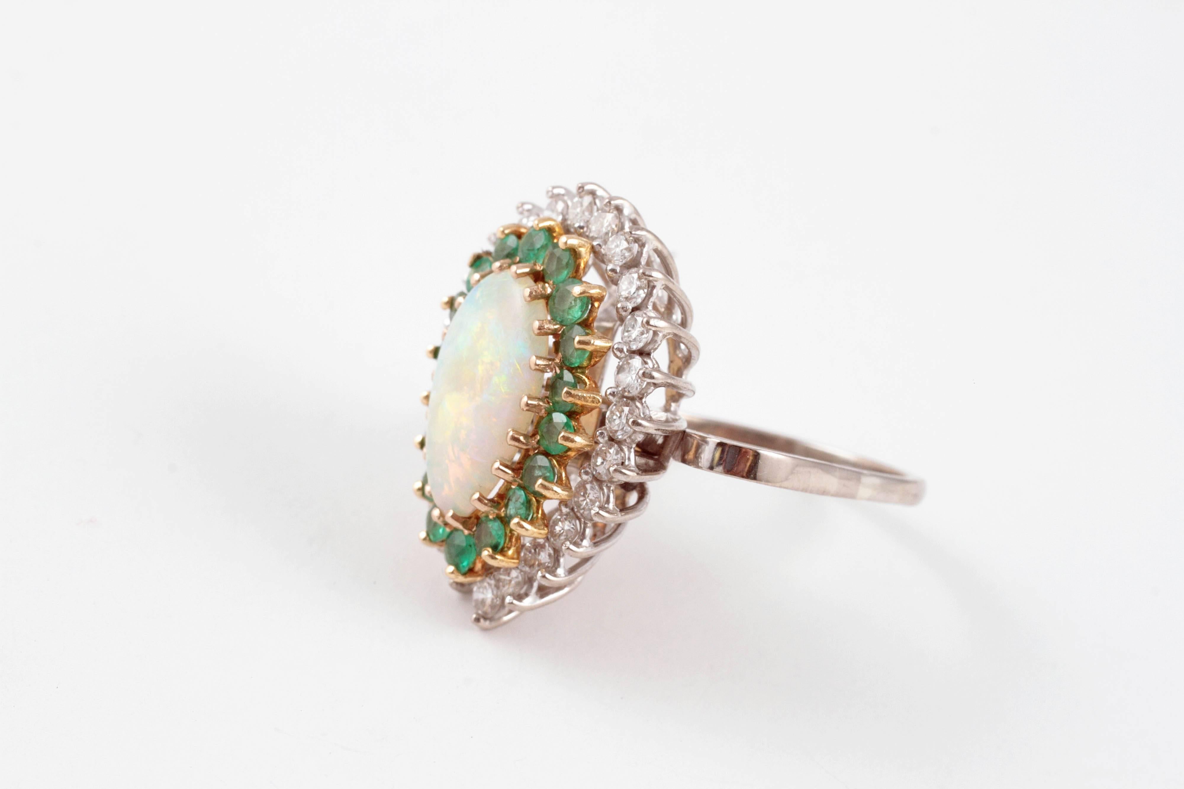 This lovely ring can be worn as a pendant too!  In 18 karat white gold, with a beautiful pear-shaped opal, surrounded by one row of emeralds and one row of diamonds. Size 9.