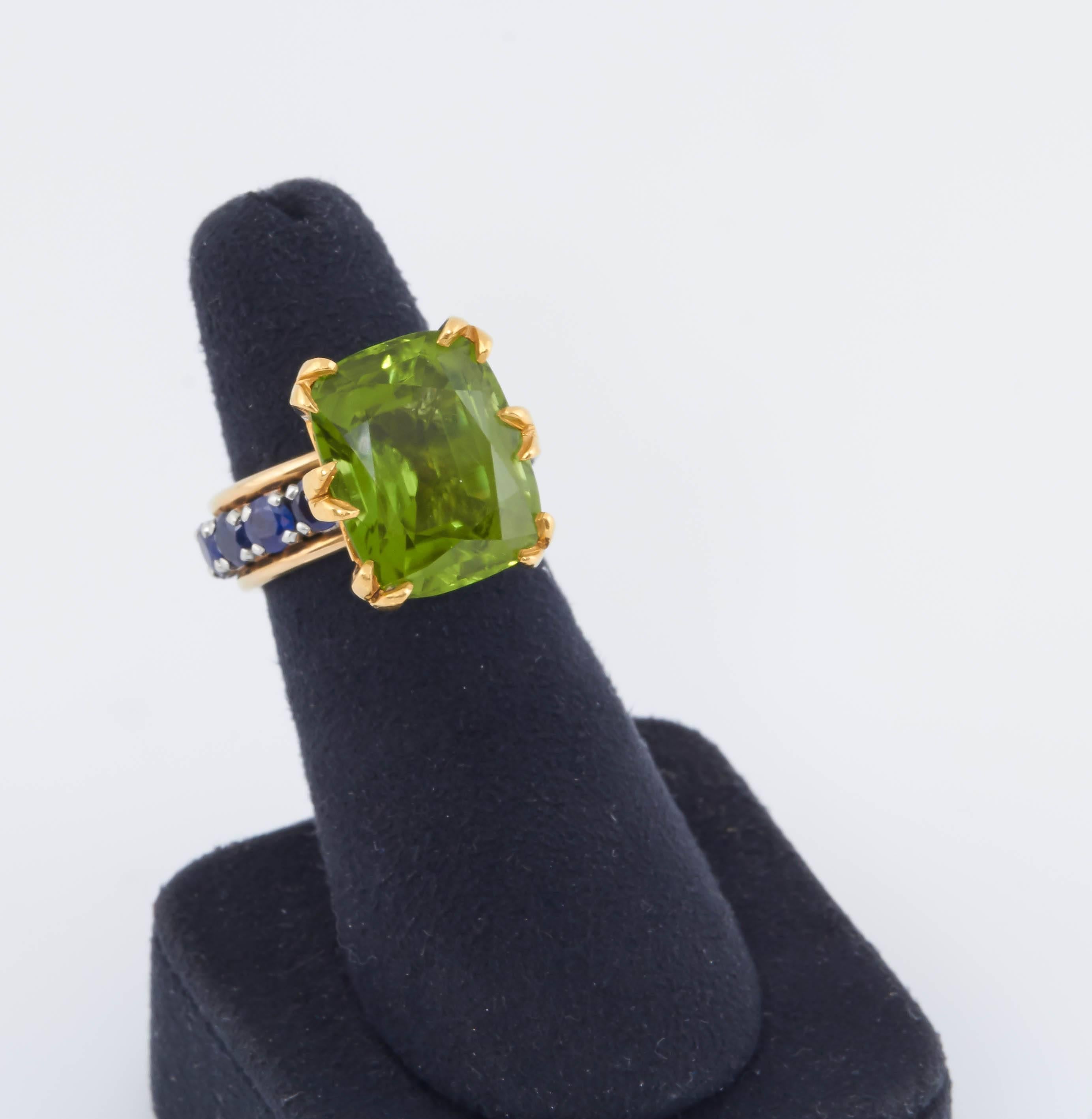 This 18K Tiffany & Co. Schlumberger Ring features a vibrant Peridot with sapphires that decorate the band all around. The ring is currently a size 5 1/4. It has a special gold spring/band inside for ring size adjustment. If the spring were to be
