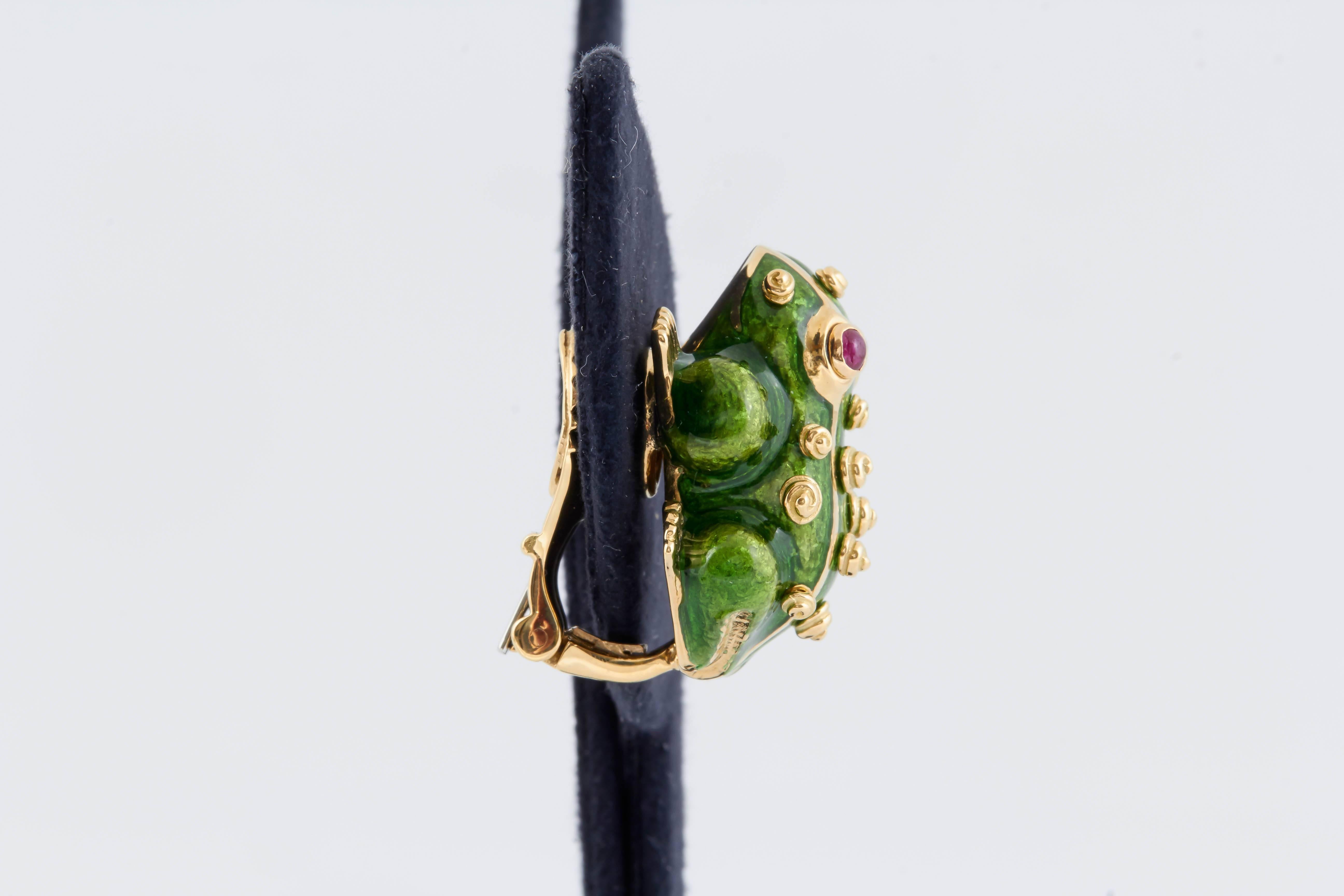 This gorgeous pair of David Webb frog earrings have been finely crafted in 18K yellow gold with a green enamel body that has raised gold "dots" throughout. Oval cabochon cut rubies for eyes accentuate this piece. The backs of the clips are