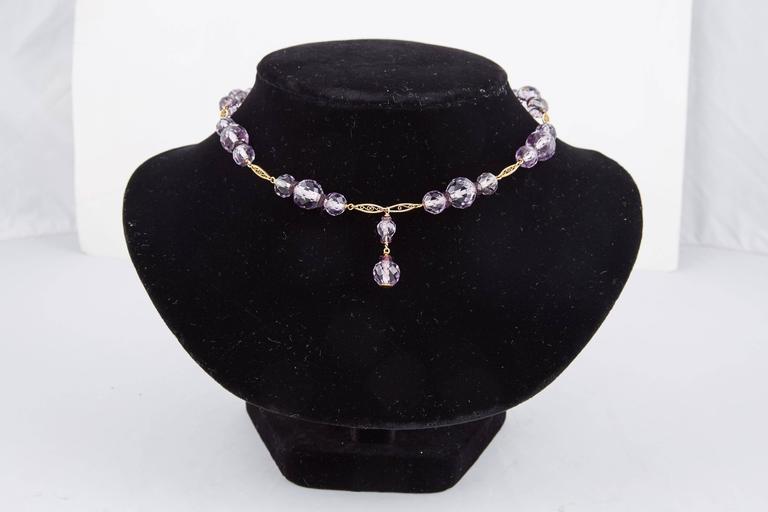 Beautiful amethyst necklace from the 1920s comprising a line of twenty-four faceted, light violet amethyst beads grouped in clusters of three, alternating with oblong gold filigree links.  Suspending two additional faceted amethyst drops, one at the