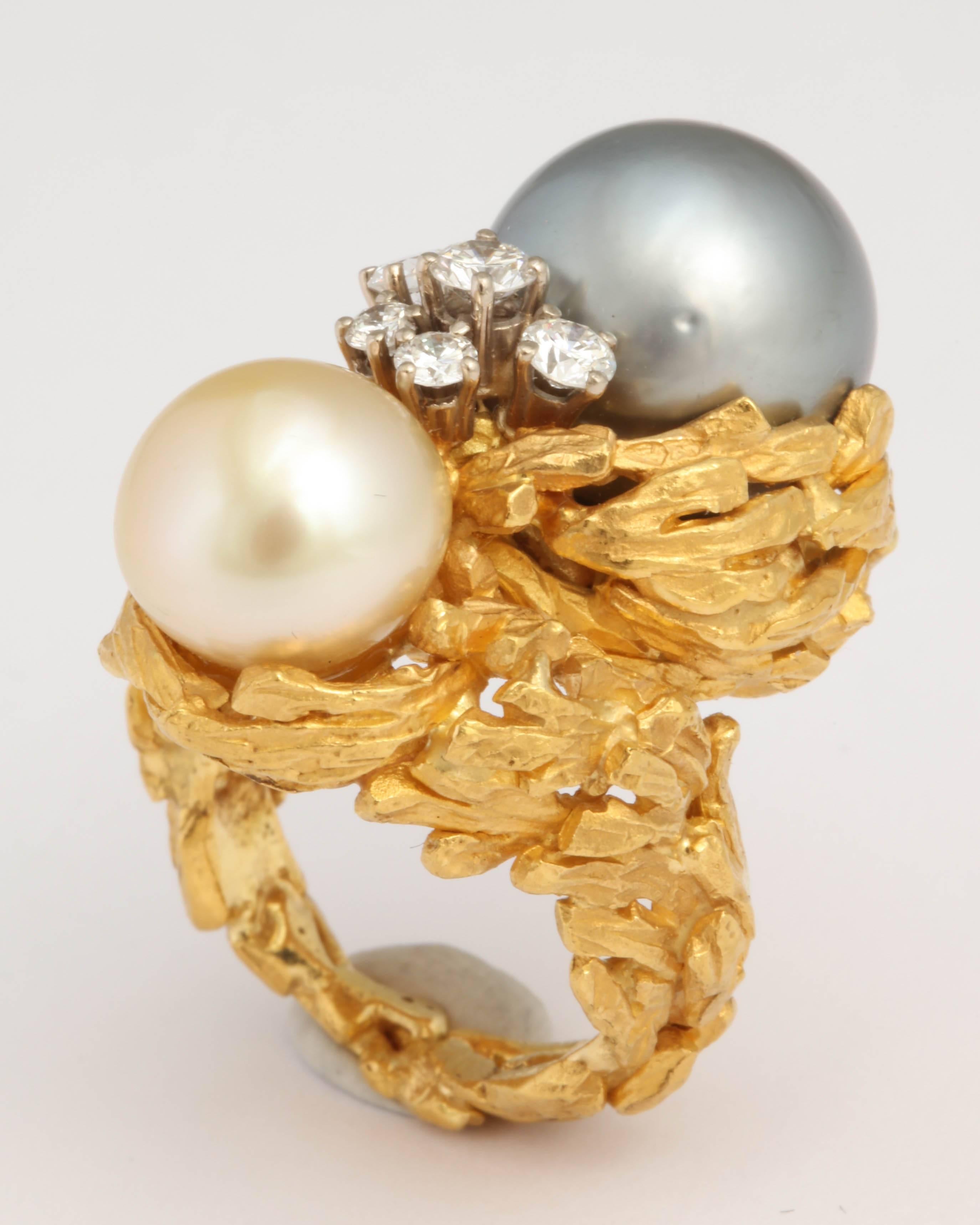 18kt Yellow Gold Double Pearl Ring - One Gray and measuring 13mm and one a creamy White measuring 10.5mm.  The Pearls are nestled in an engraved Foliate setting that encompasses the whole Ring.  Between the two Pearls are 5 prong set Diamonds, which