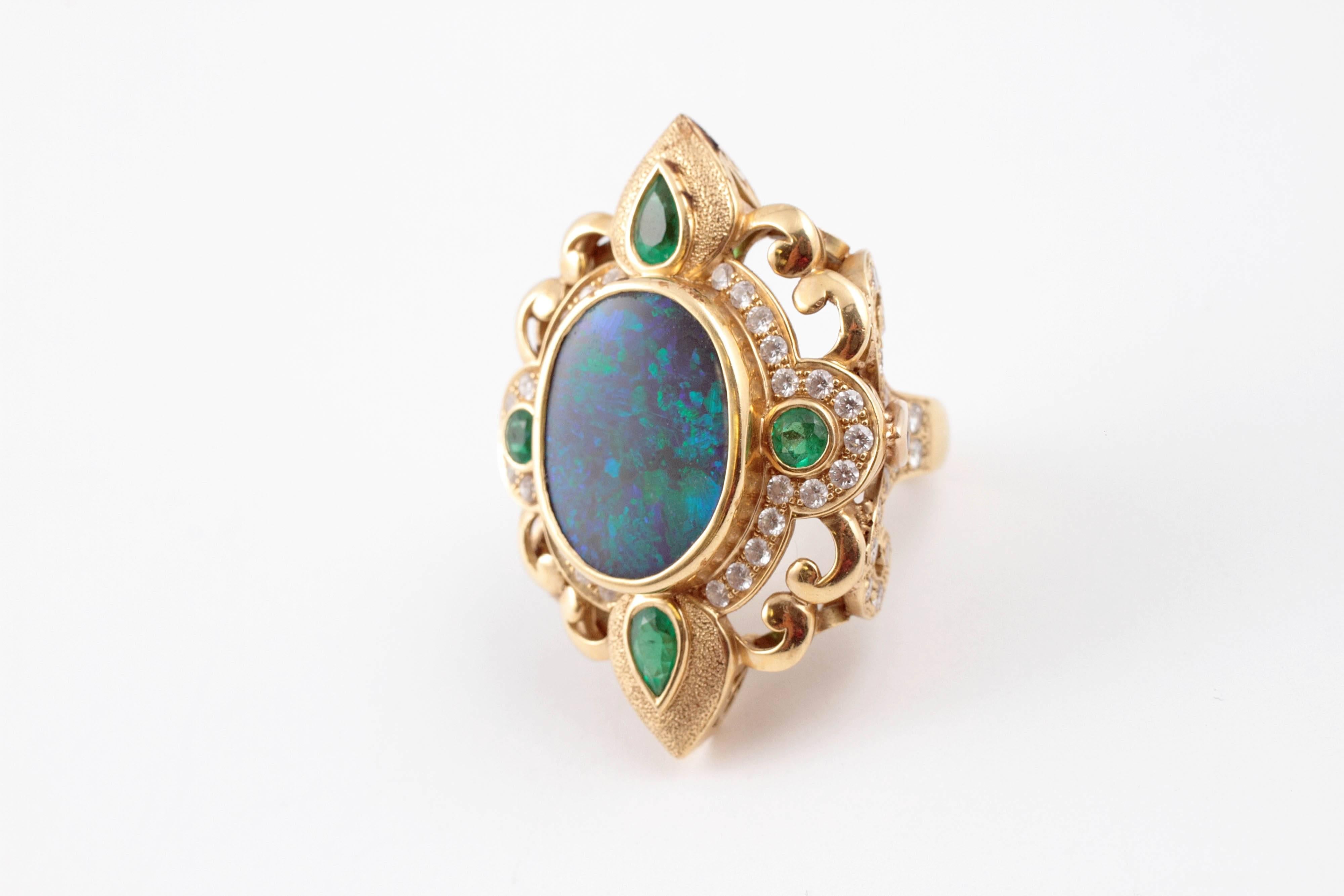 Boldly beautiful in green and blue opal.  Crevoshay's 7.33 carat black opal ring with stunning fire accented by 1.08 carats of emeralds and .74 carats of diamonds in 18 Karat yellow gold. Size 8.25. Sides are encrusted with diamonds.  
