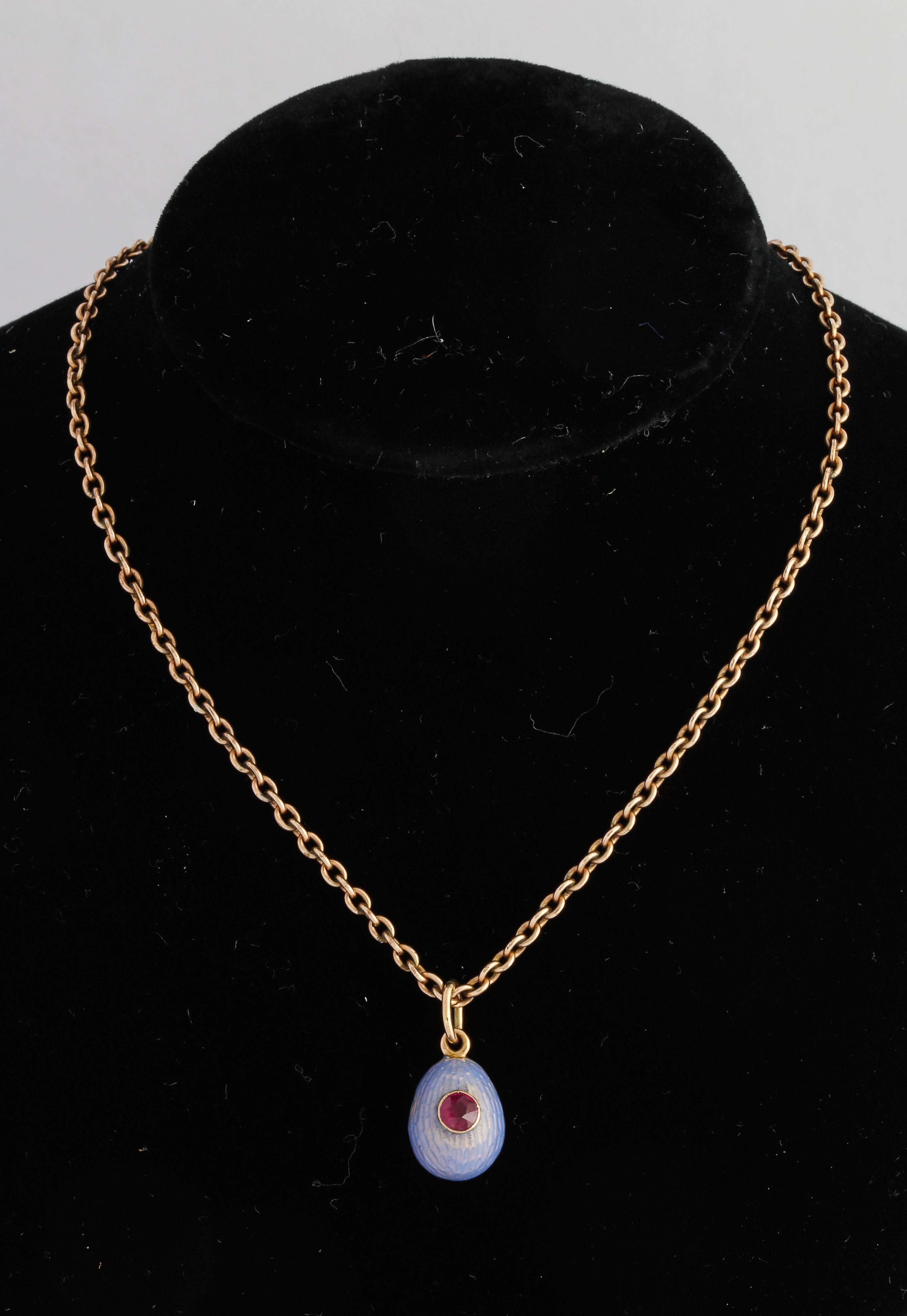Set with a circular-cut ruby, surrounded by light blue translucent enamel on a gold ground, attached to a gold suspension ring. Chain not included.