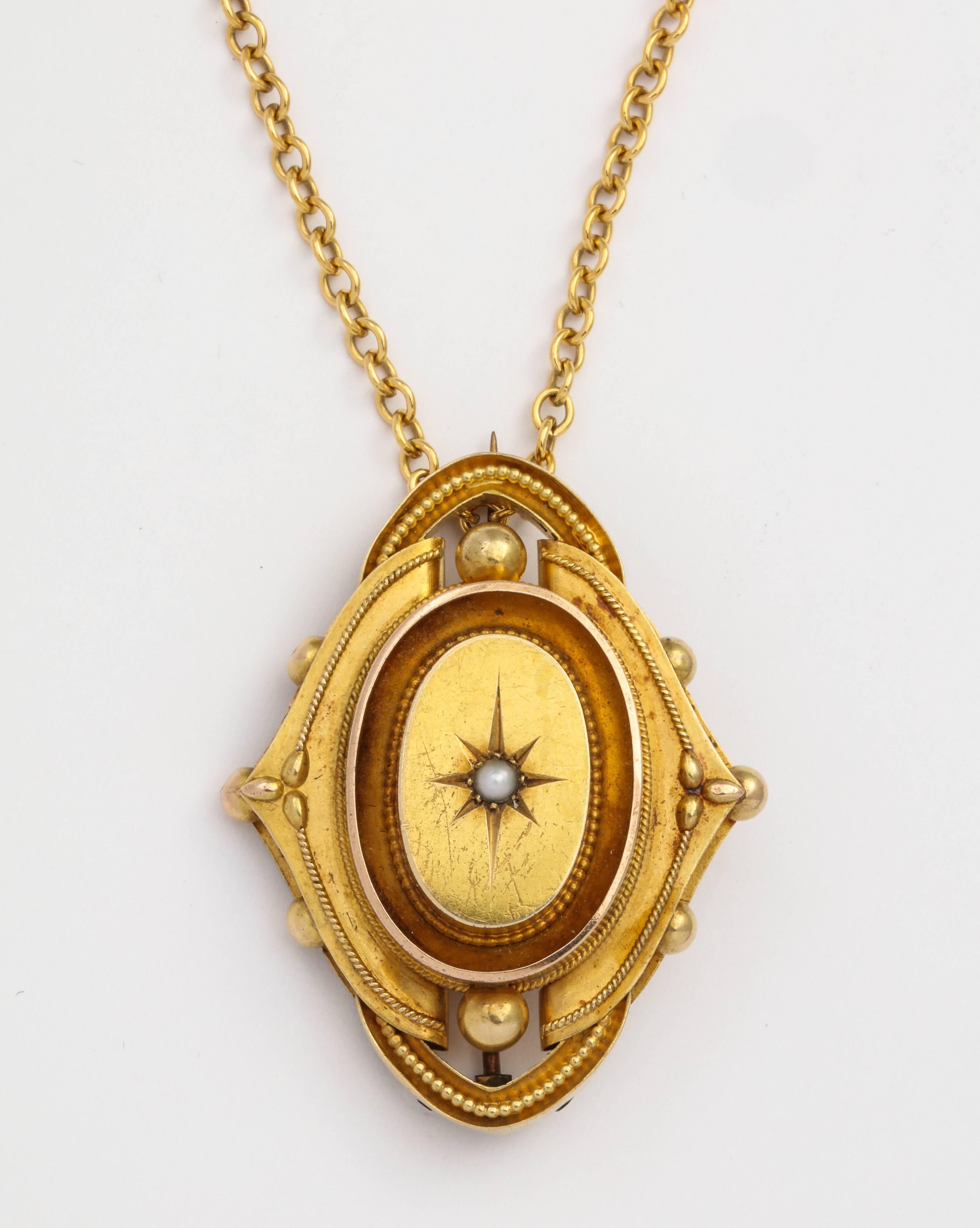 From the mid-Victorian era, a gold Etruscan Revival memorial pin, the raised center enhanced with a seed pearl in a starburst setting within beaded gold borders. The reverse is fitted with a glass-covered compartment for a photo or lock of hair. Can