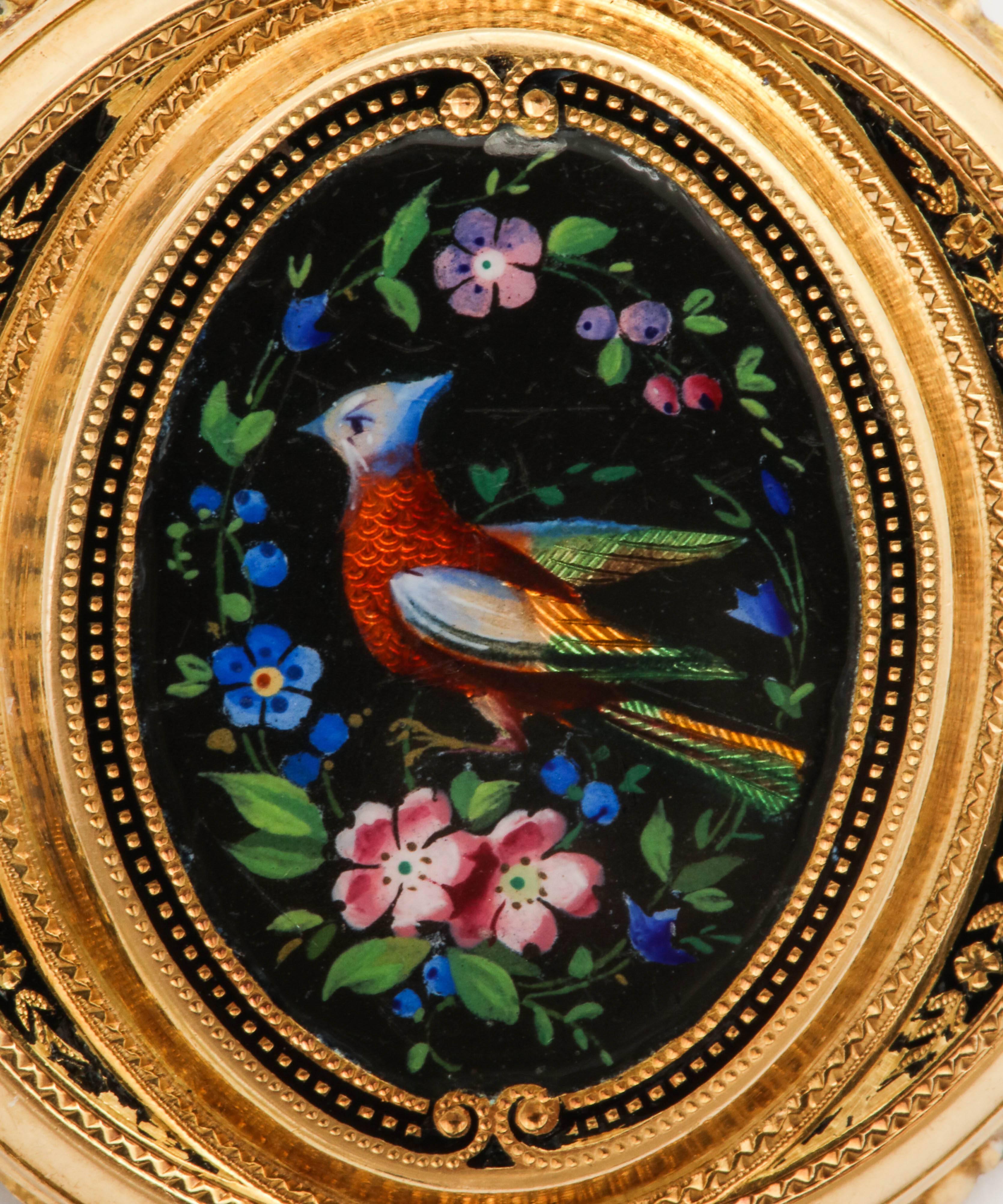 Colorful painted enamel Bird of Paradise gold Pin/endant, circa 1870, of 18k gold, depicting a vibrantly colored bird in translucent enamel amidst dense clusters of violet and pink flowers, on a black enamelled ground, enhanced by black and gold