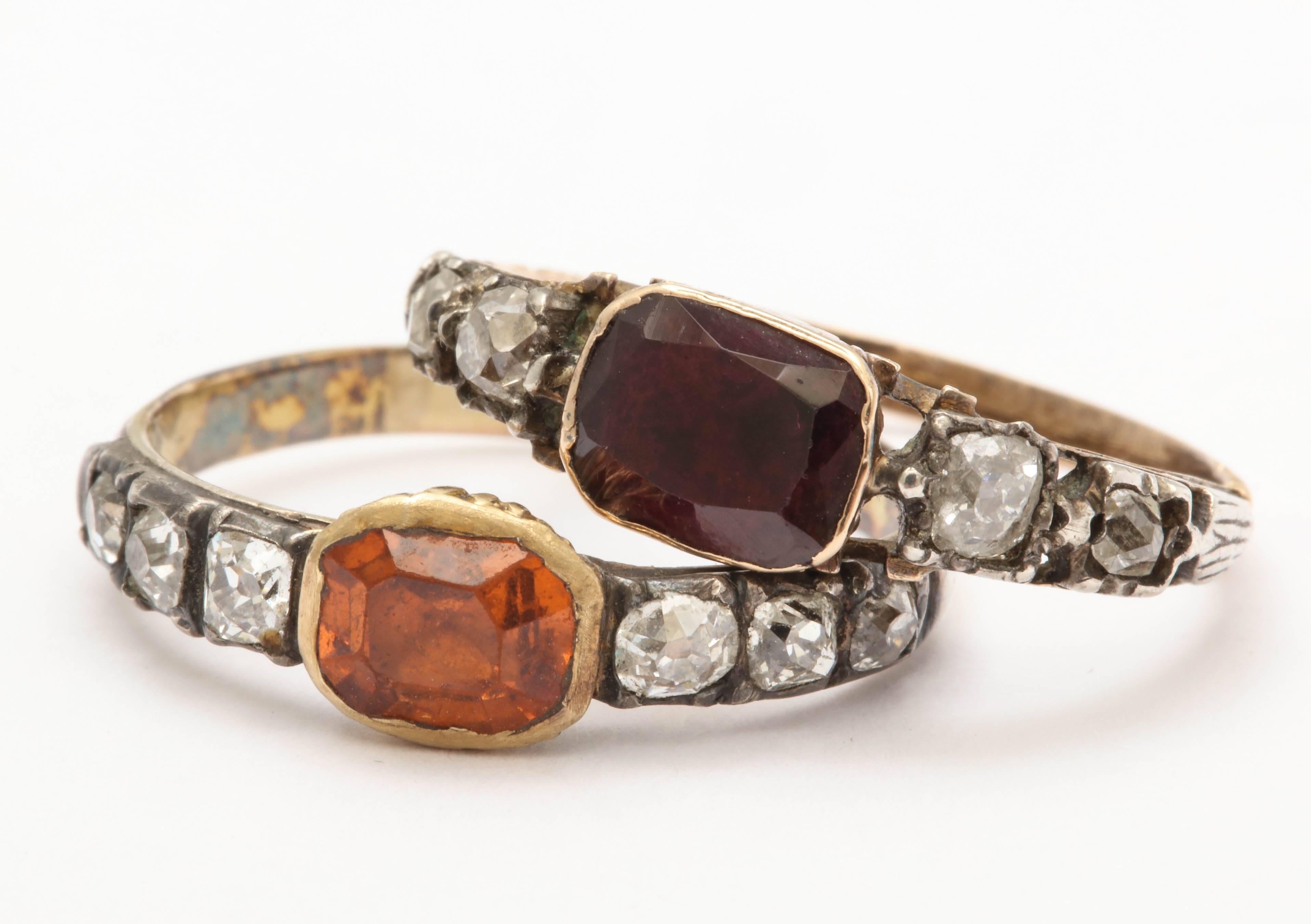 A beautiful duo of nearly matched Georgian era rings. Both closed back and set in silver over yellow gold. One is set with a garnet and flanked by two diamonds on either side. The other is set with a hessonite flanked with three diamonds on either