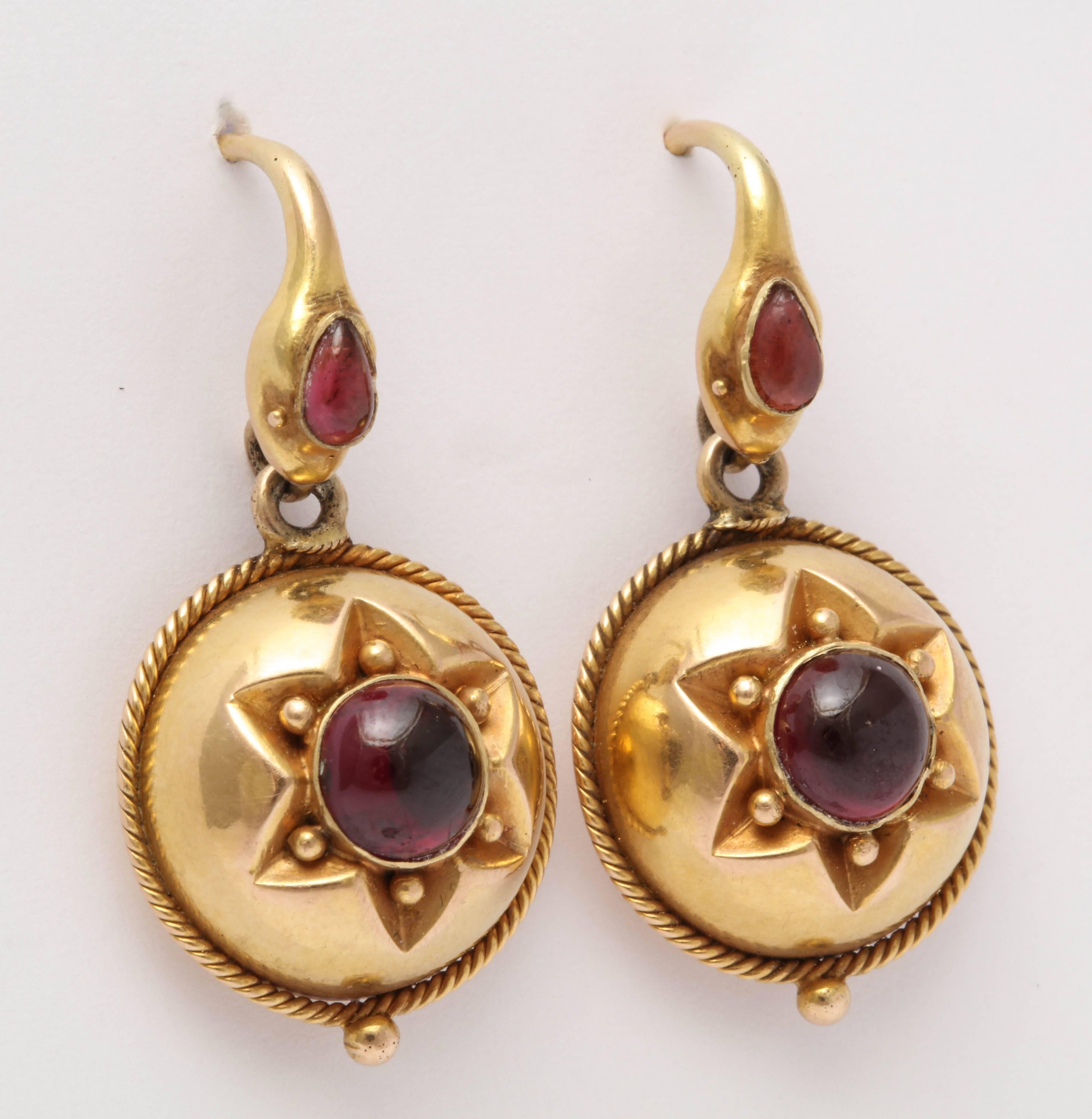 A whimsical example of Victorian snake symbolism. These lovely dangle earrings are topped with a snake's head. The heads are set with a pear shaped garnet. Below is a round cabochon garnet set in a star design in round yellow gold bulbous disk with