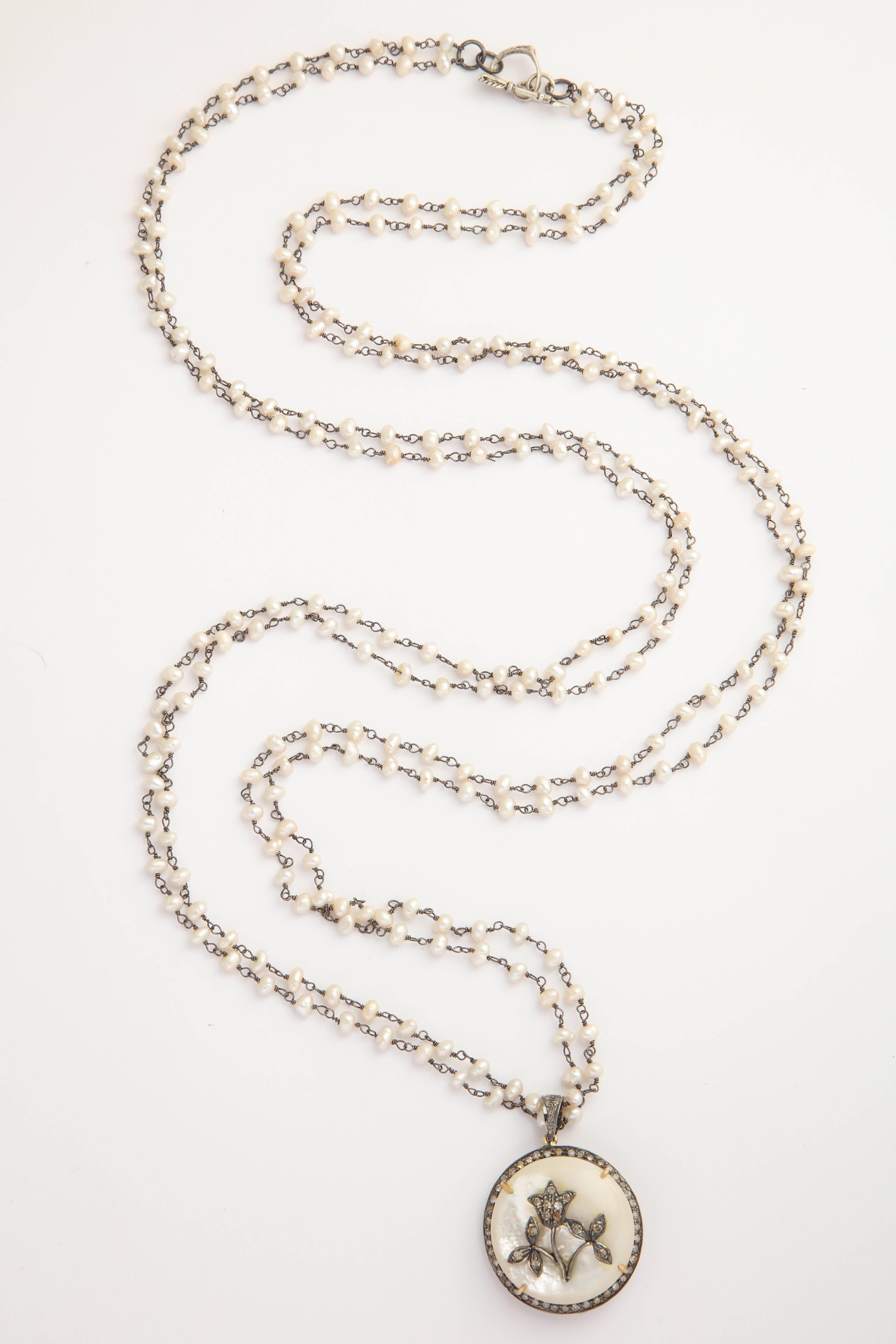 This elegant and stylish necklace is two strands of 40 inch freshwater pearl chain.  The pendant is a large dome of Mother of Pearl surrounded by diamonds with a silver and diamond floral center. It can be worn twice around the neck and settle at