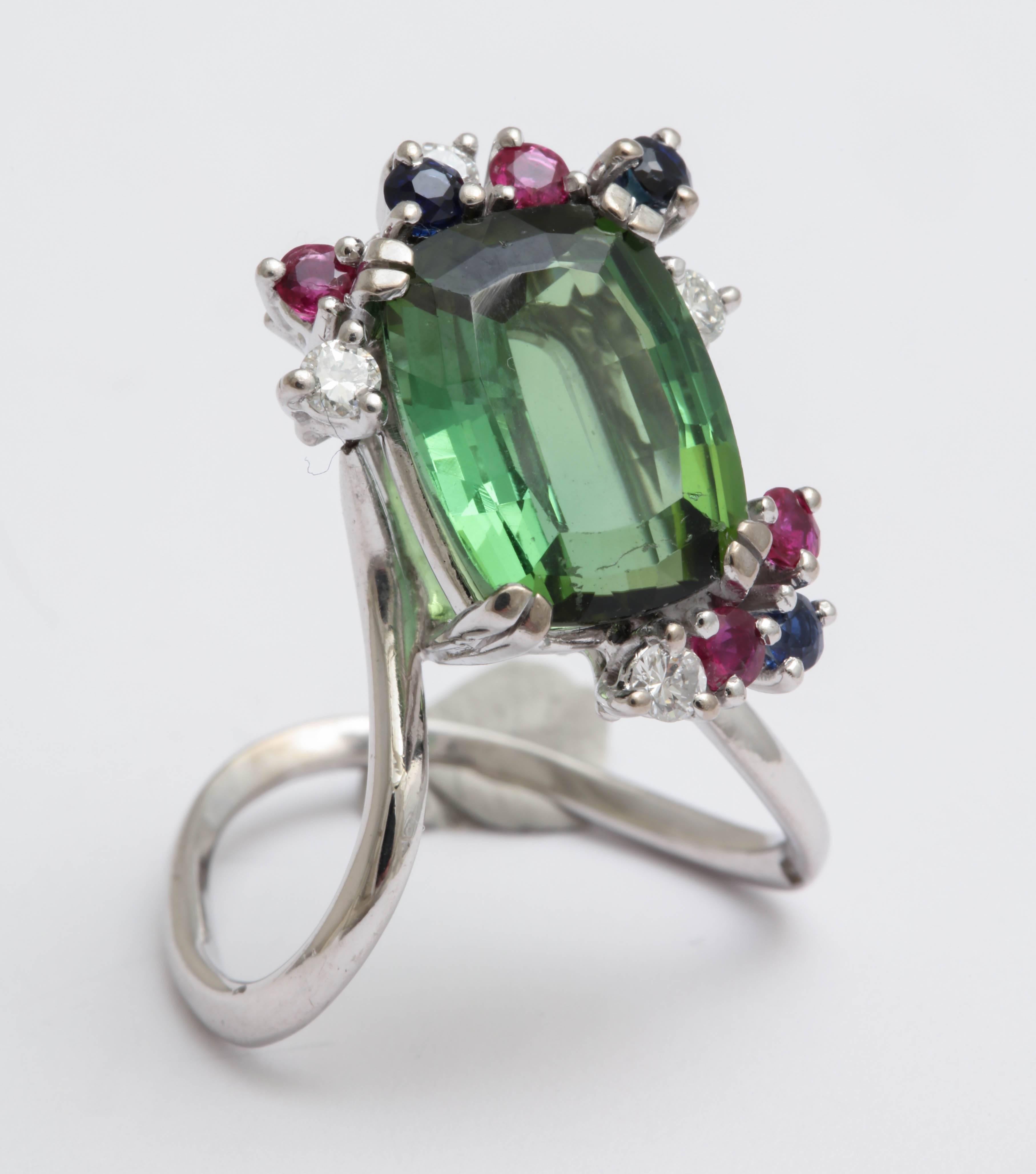 Modernist 18kt white gold Ring set with a faceted cushion cut Green Tourmaline and edged with Rubies, Diamonds and Sapphires.  Superb quality stones and unusual design.  Signed with the Stern trademark.  Tourmaline 13mmx10x6mm  