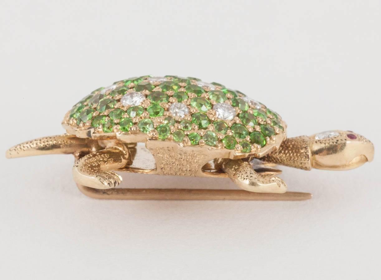 An 18 karat yellow gold brooch in the form of a Tortoise. The shell of the tortoise is pave set with fine quality green garnets and brilliant cut diamonds with diamonds also set to the head and contrasting ruby eyes.
Measures 32mm in length x 16mm