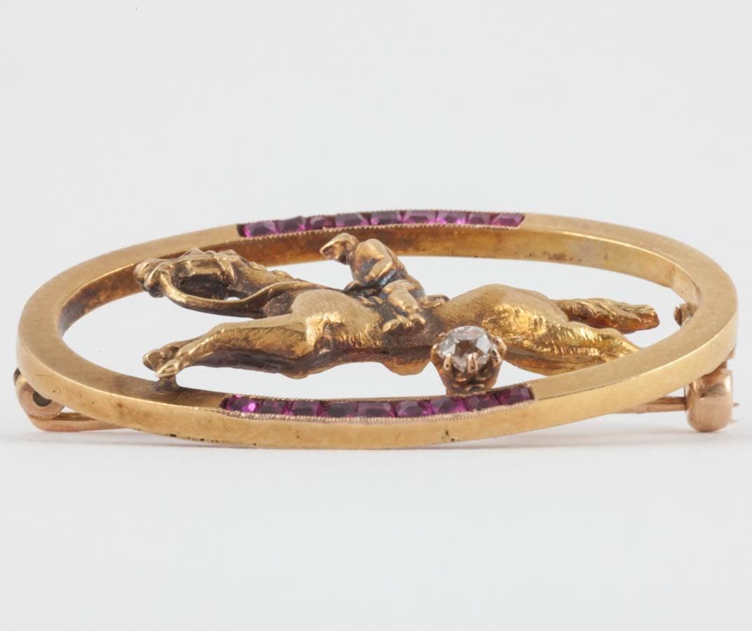 An oval 18ct gold brooch set with calibre cut Burma rubies,the centre with a racehorse and jockey,and a single,old cut diamond as the winning post.English c,1900