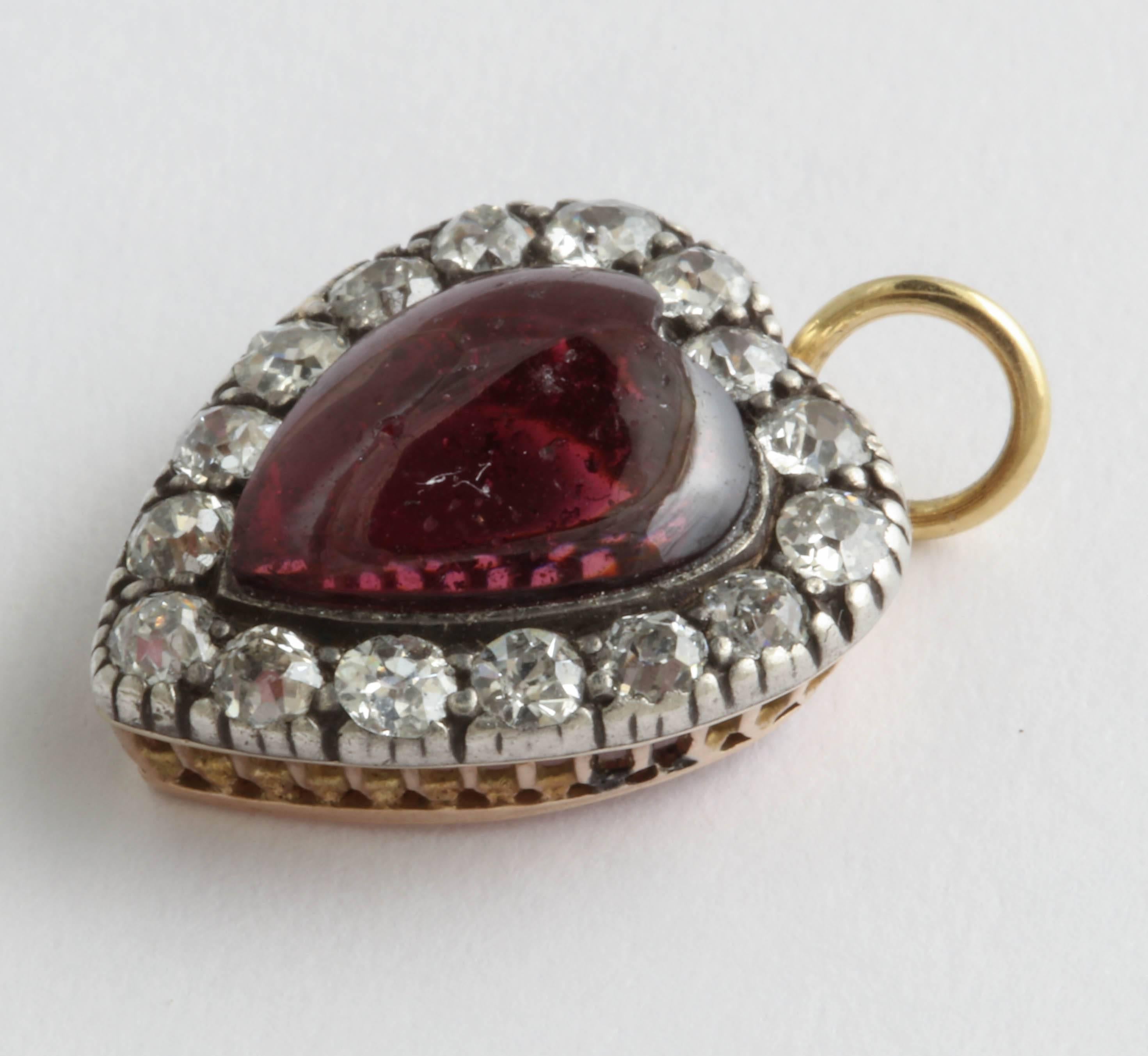 Cabochon garnet heart is surrounded by 16 old mine cut diamonds. Diamonds are over .75 total carat weight. Set in silver over yellow gold. 