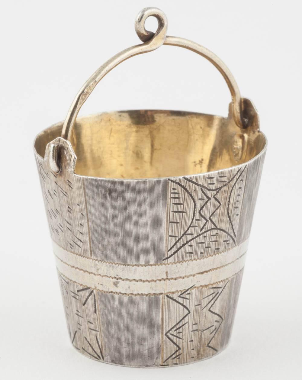 From the Romanov era, period of tsar Alexander III, the tapered silver bucket engraved on the exterior and gilded on base and interior, attached to a swing handle which was used to balance over a tea cup from a silver harness (missing). Sold as is.